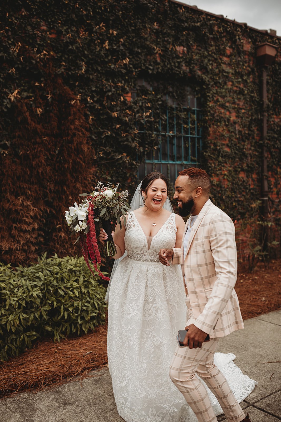 Bride and groom posing in front of the signature green ivy wall at Studio 215 in downtown Fayetteville, NC; a lush urban garden photography backdrop at our industrial warehouse venue near Fort Bragg and Raleigh.