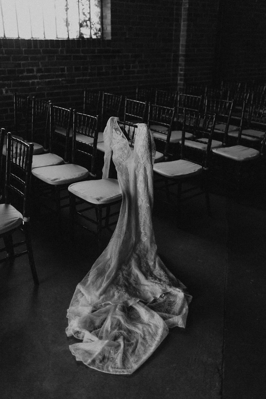 A wedding dress draped over a chair in an empty, dark room with multiple chairs arranged in rows.