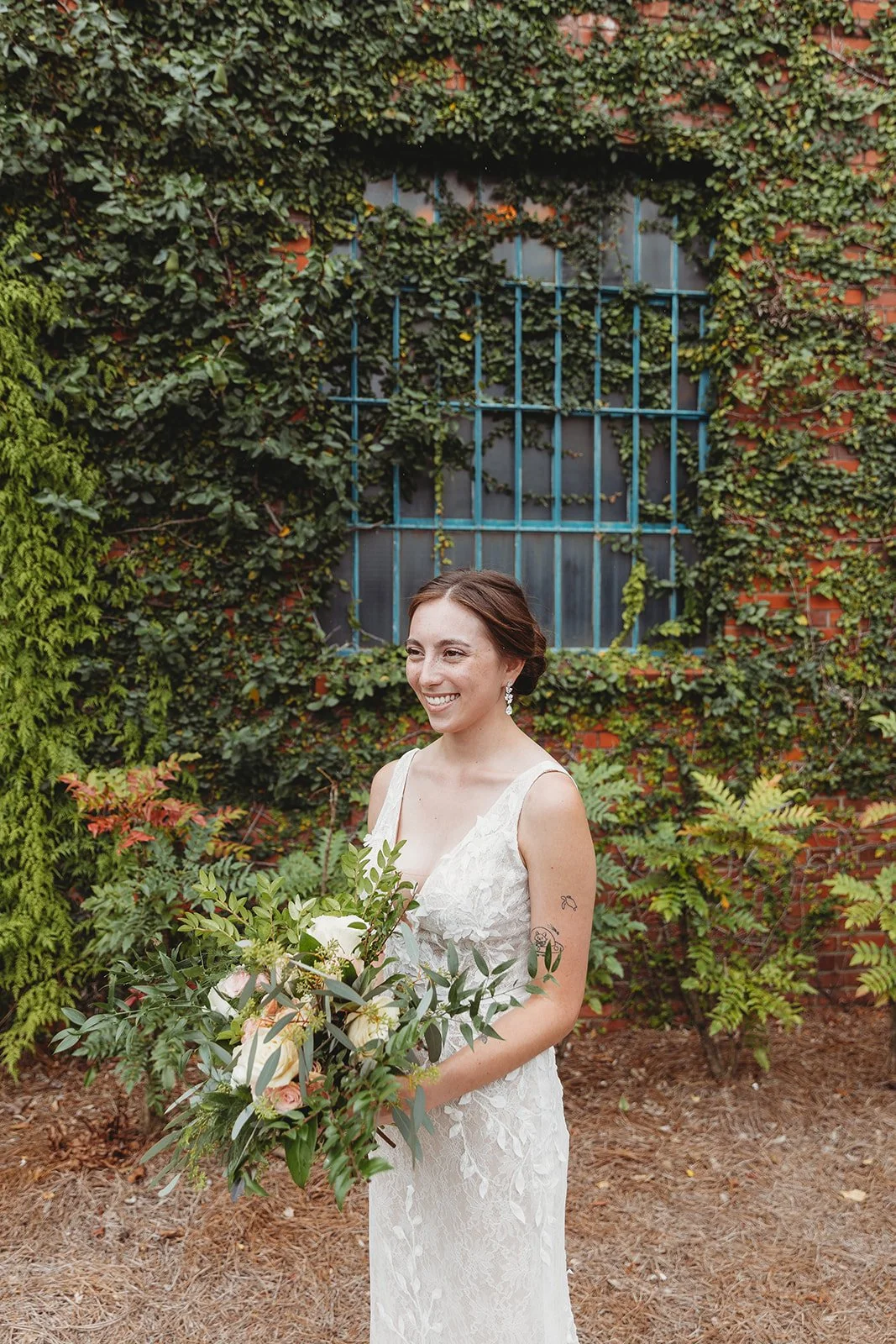 Bride and groom posing in front of the signature green ivy wall at Studio 215 in downtown Fayetteville, NC; a lush urban garden photography backdrop at our industrial warehouse venue near Fort Bragg and Raleigh.