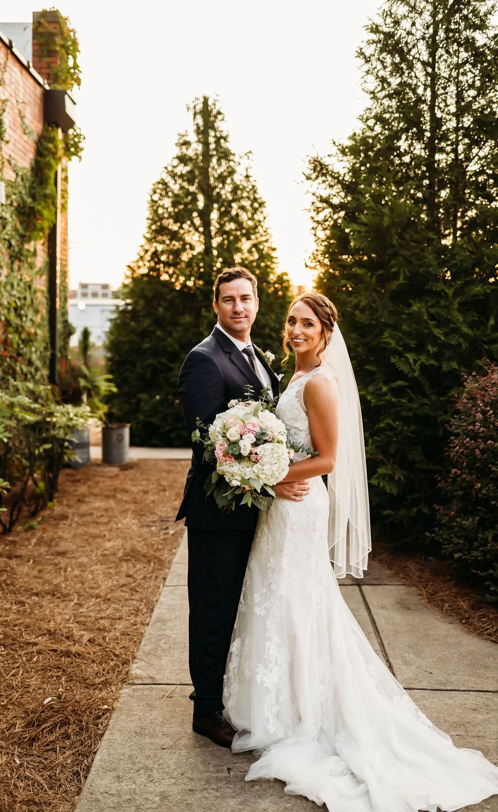 Bride and groom posing in front of the signature green ivy wall at Studio 215 in downtown Fayetteville, NC; a lush urban garden photography backdrop at our industrial warehouse venue near Fort Bragg and Raleigh.