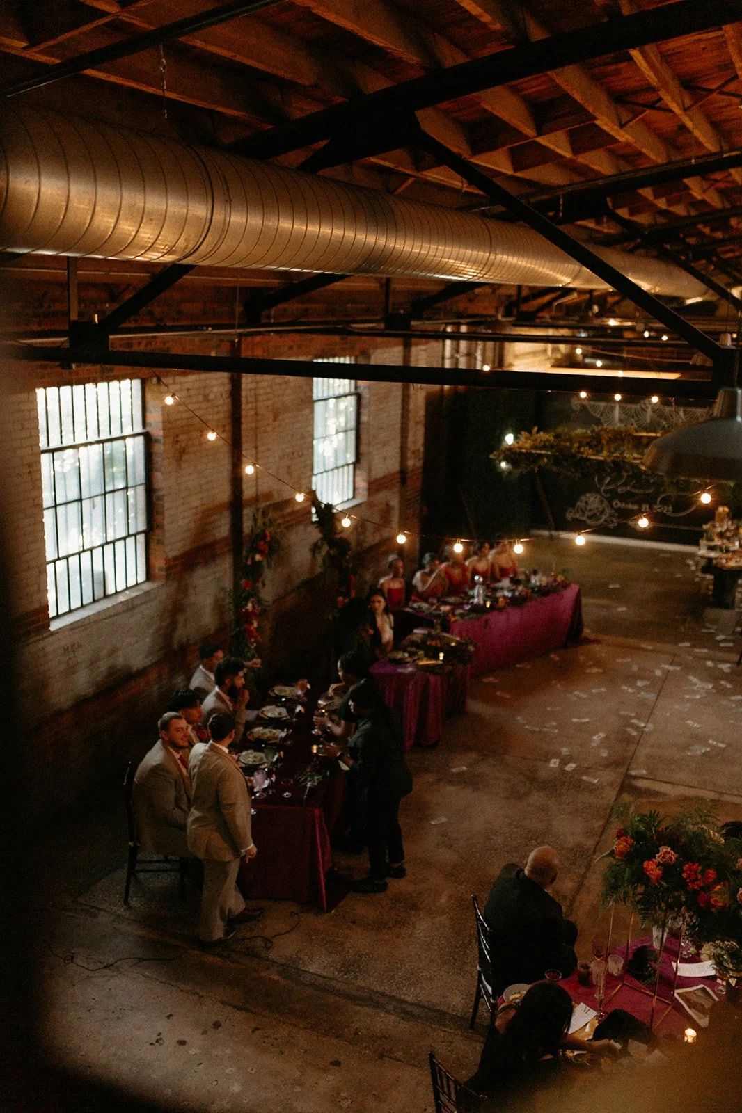 People gathered for a celebration or dinner in a rustic, industrial-style venue with exposed brick walls and string lights.