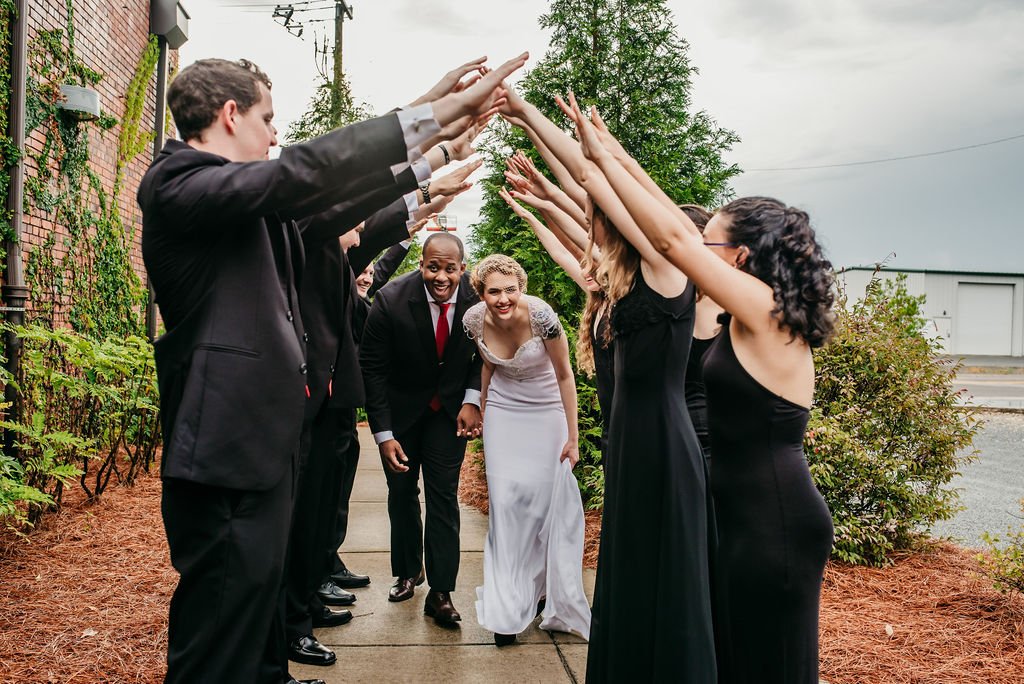 Bride and groom posing in front of the signature green ivy wall at Studio 215 in downtown Fayetteville, NC; a lush urban garden photography backdrop at our industrial warehouse venue near Fort Bragg and Raleigh.