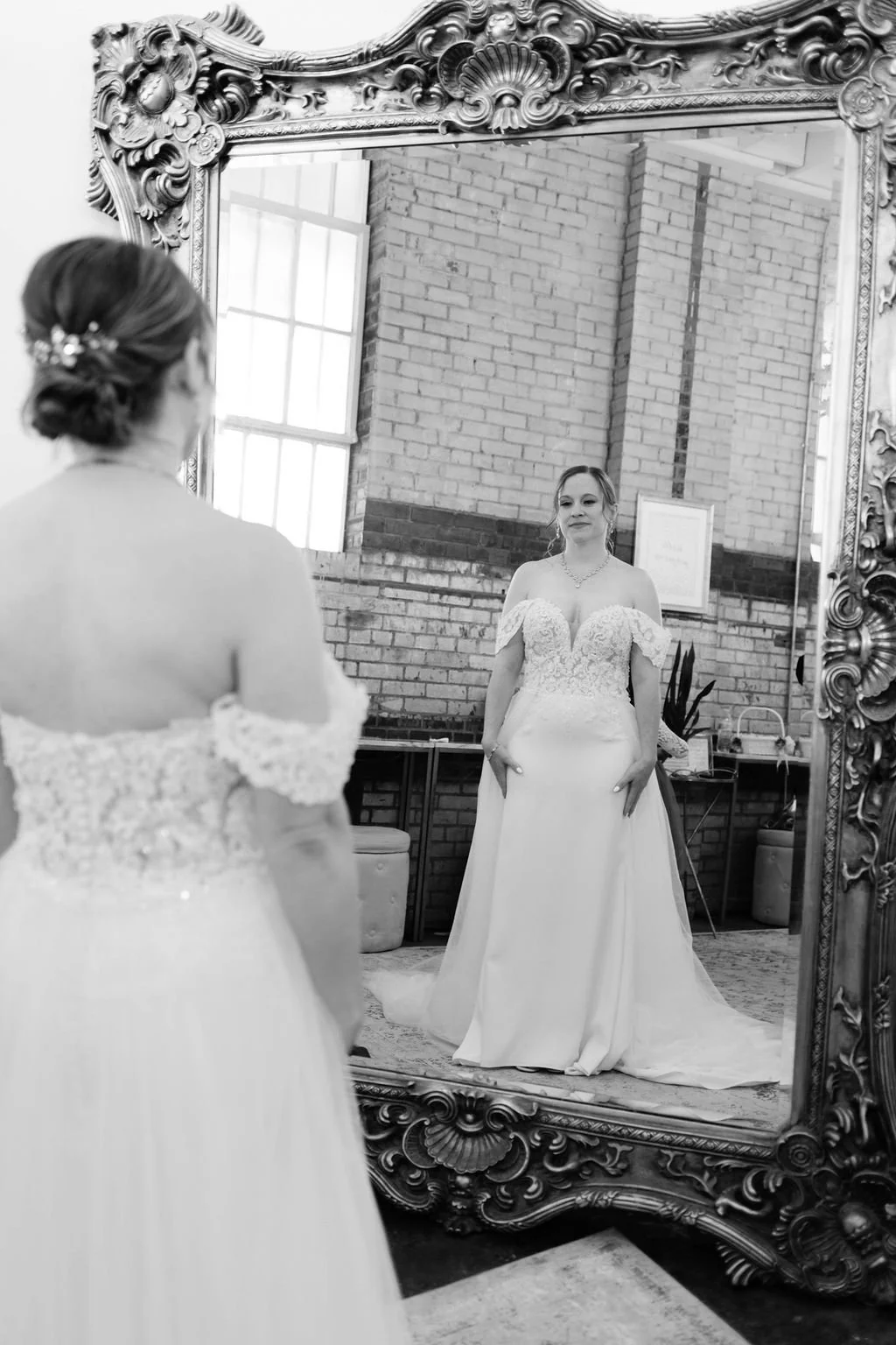 A bride in a wedding dress is looking at herself in an ornate mirror at Studio 215 a modern warehouse venue in Fayetteville, NC