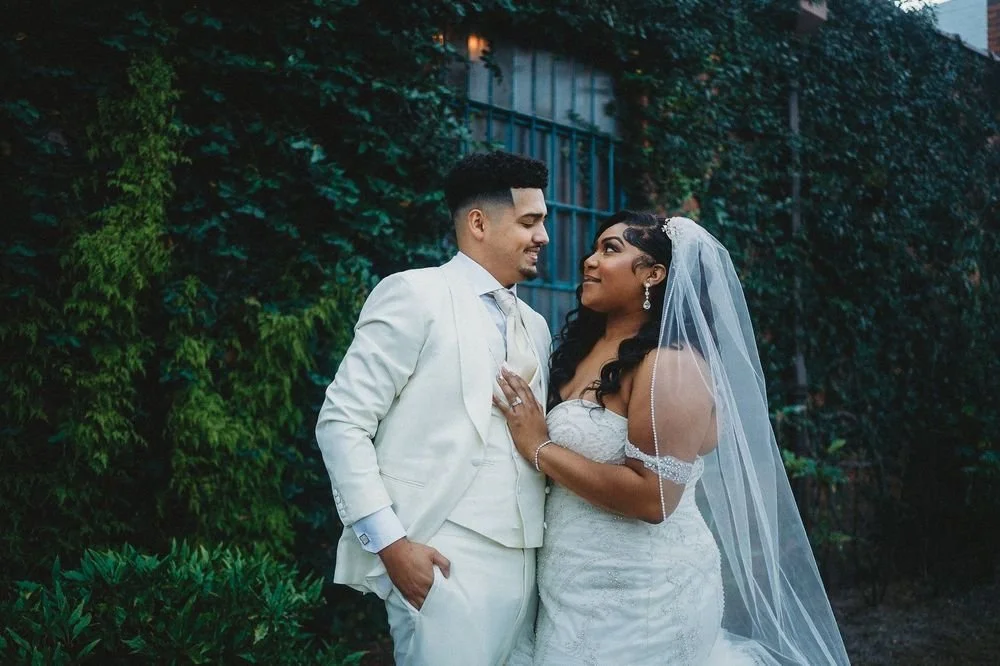 Bride and groom posing in front of the signature green ivy wall at Studio 215 in downtown Fayetteville, NC; a lush urban garden photography backdrop at our industrial warehouse venue near Fort Bragg and Raleigh.