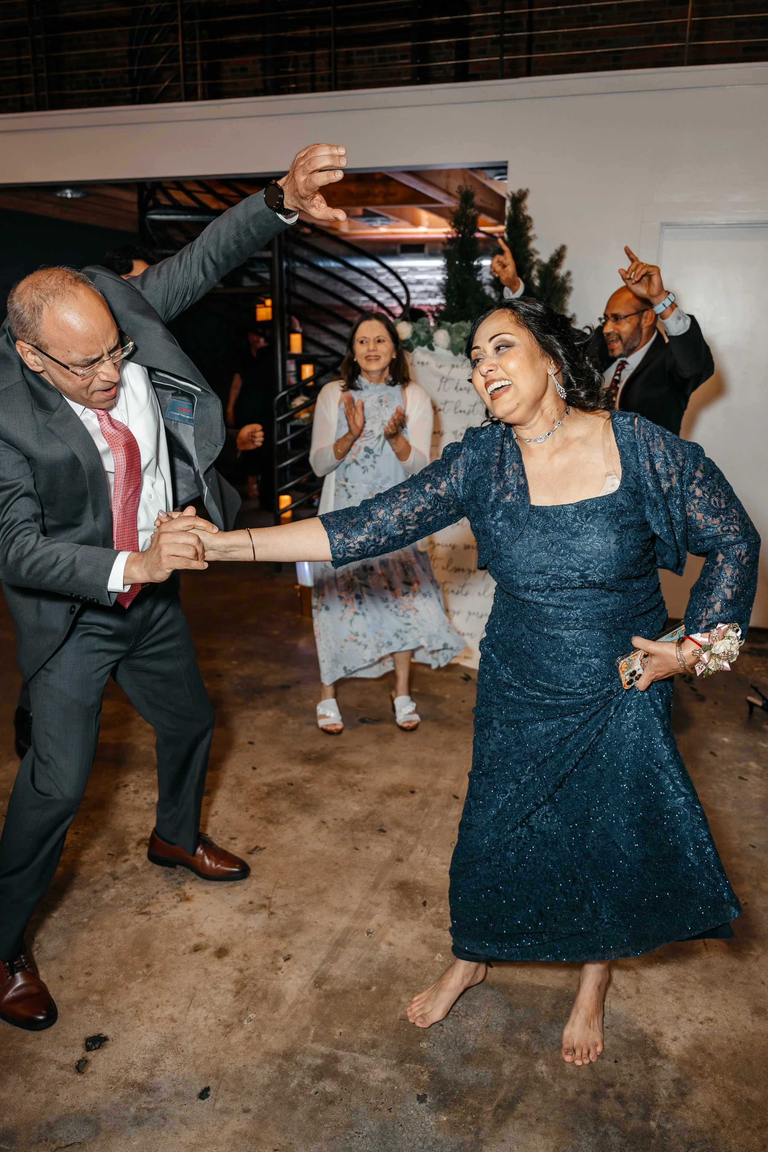 People dancing and celebrating at a festive event, with a woman in a navy blue dress dancing barefoot.
