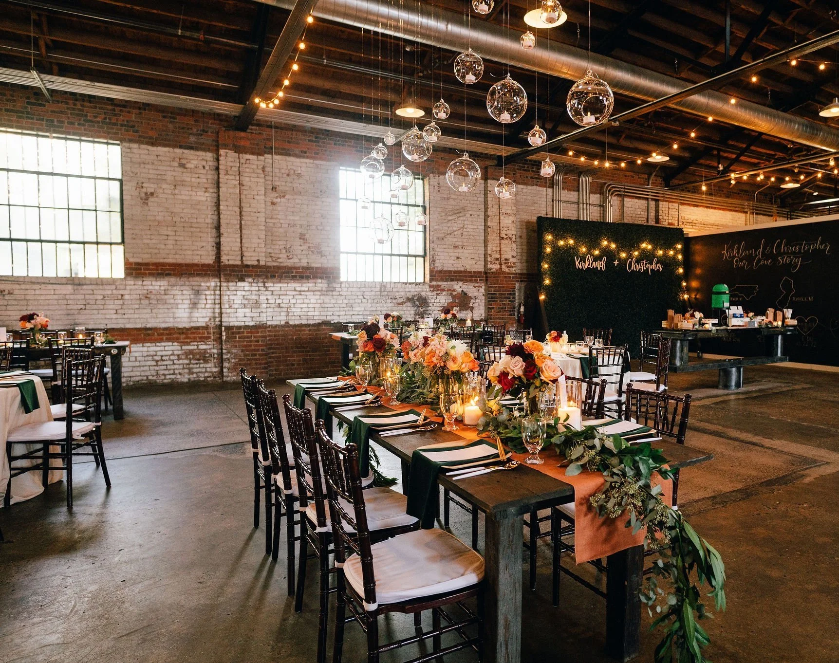 Wedding reception table setup with floral centerpieces and candles in a rustic venue with exposed brick walls and string lights.