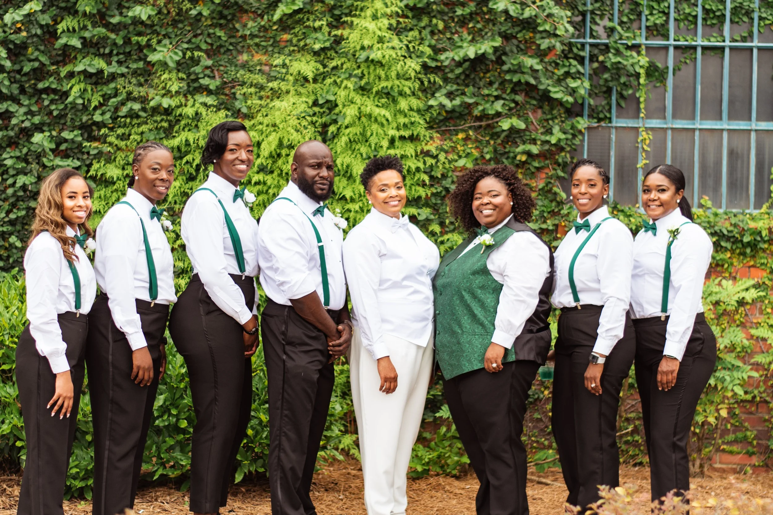 Bride and groom posing in front of the signature green ivy wall at Studio 215 in downtown Fayetteville, NC; a lush urban garden photography backdrop at our industrial warehouse venue near Fort Bragg and Raleigh.