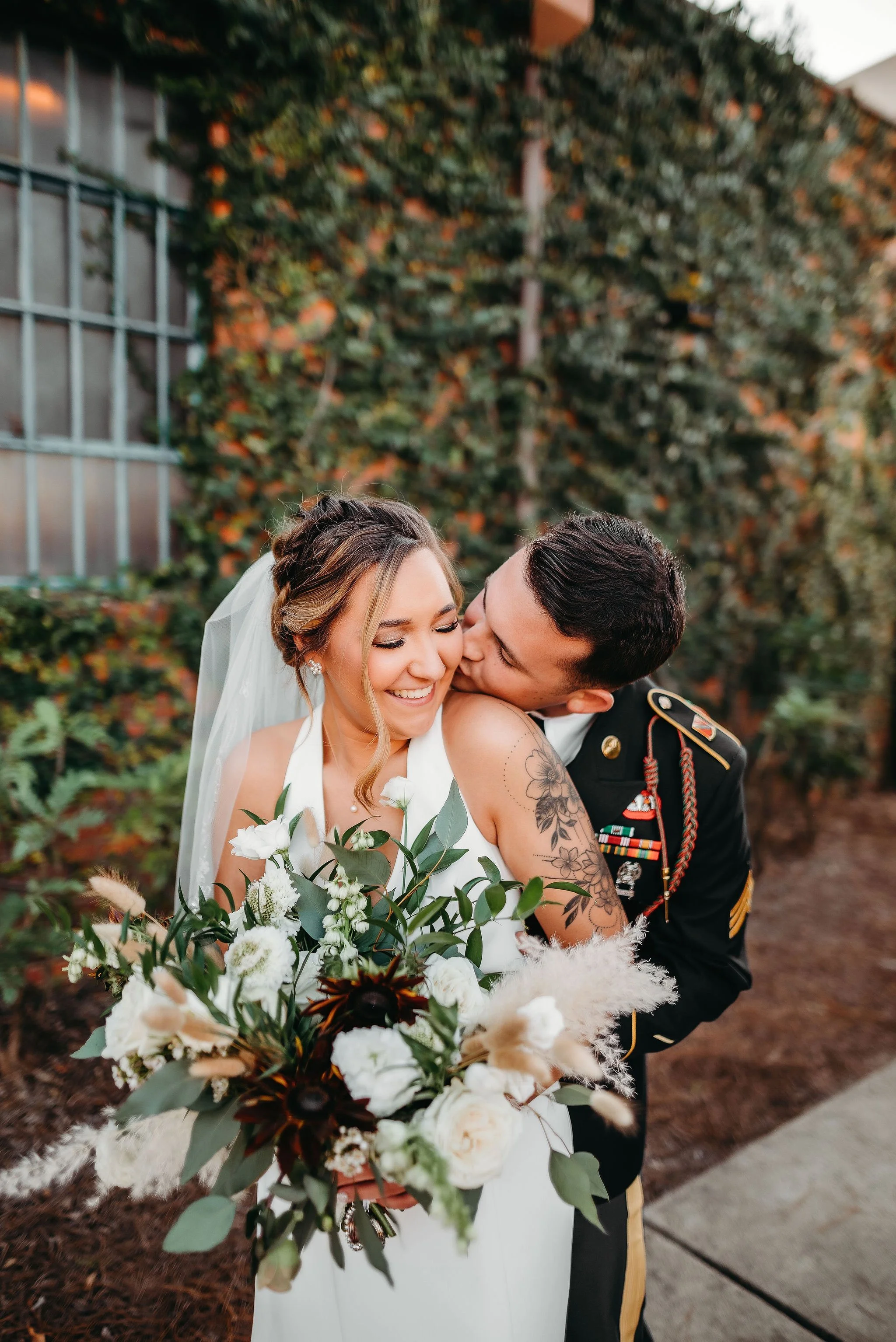 Bride and groom posing in front of the signature green ivy wall at Studio 215 in downtown Fayetteville, NC; a lush urban garden photography backdrop at our industrial warehouse venue near Fort Bragg and Raleigh.