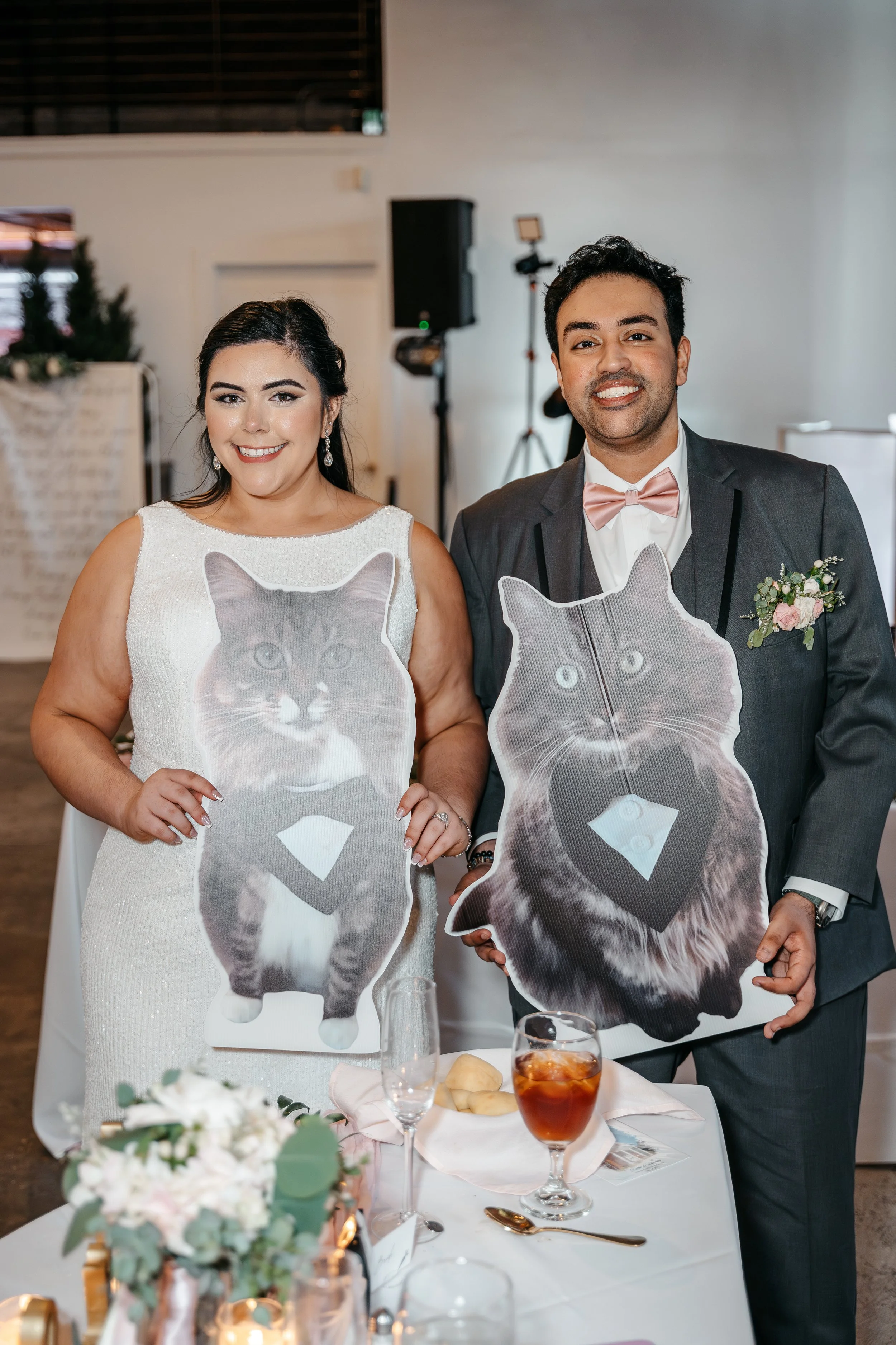 A bride and groom holding cardboard cutouts of cats at a wedding reception.