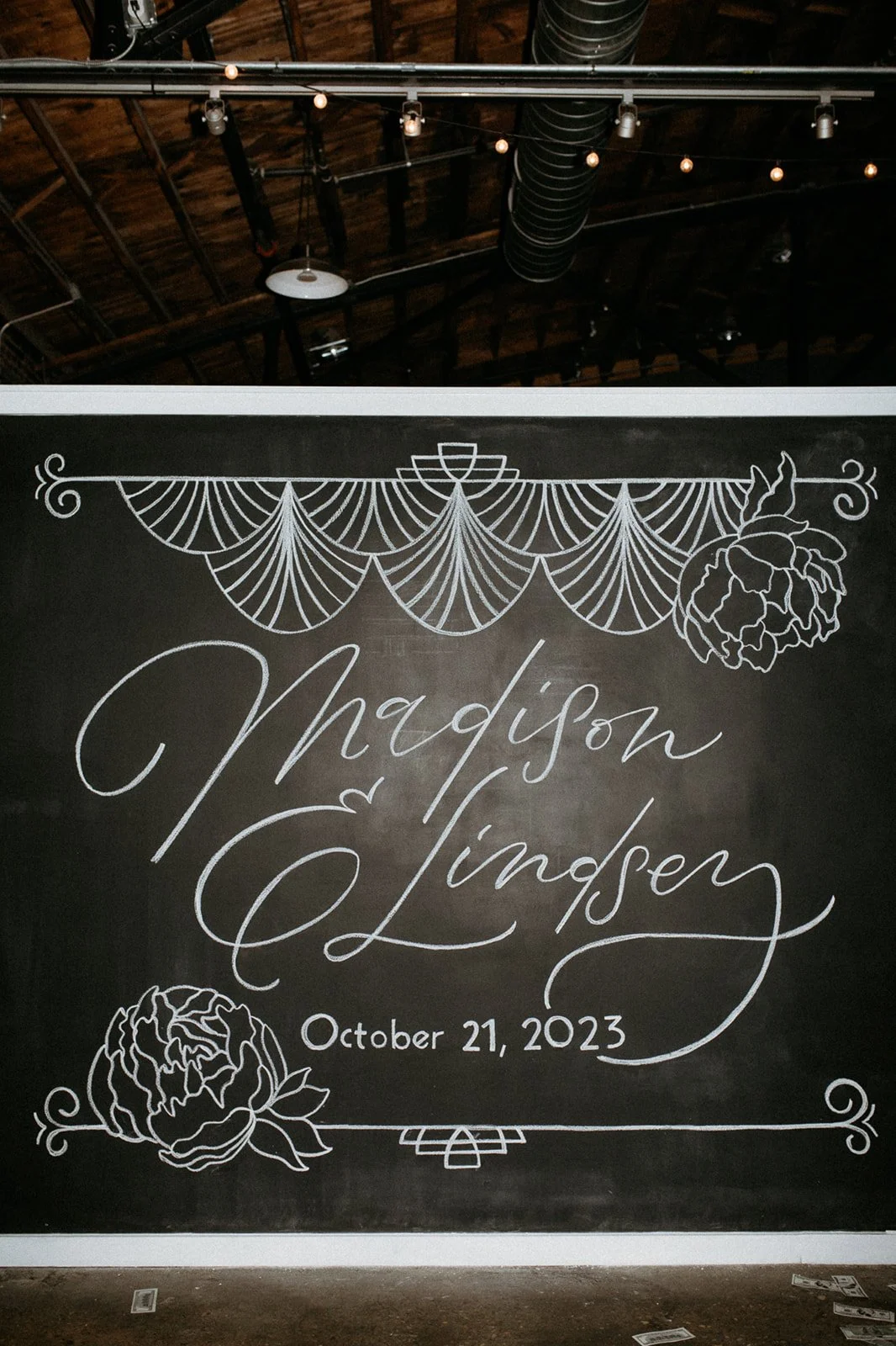 Chalkboard-style wedding sign with floral and decorative designs, displaying the names Madison and Linden and the date October 21, 2023.