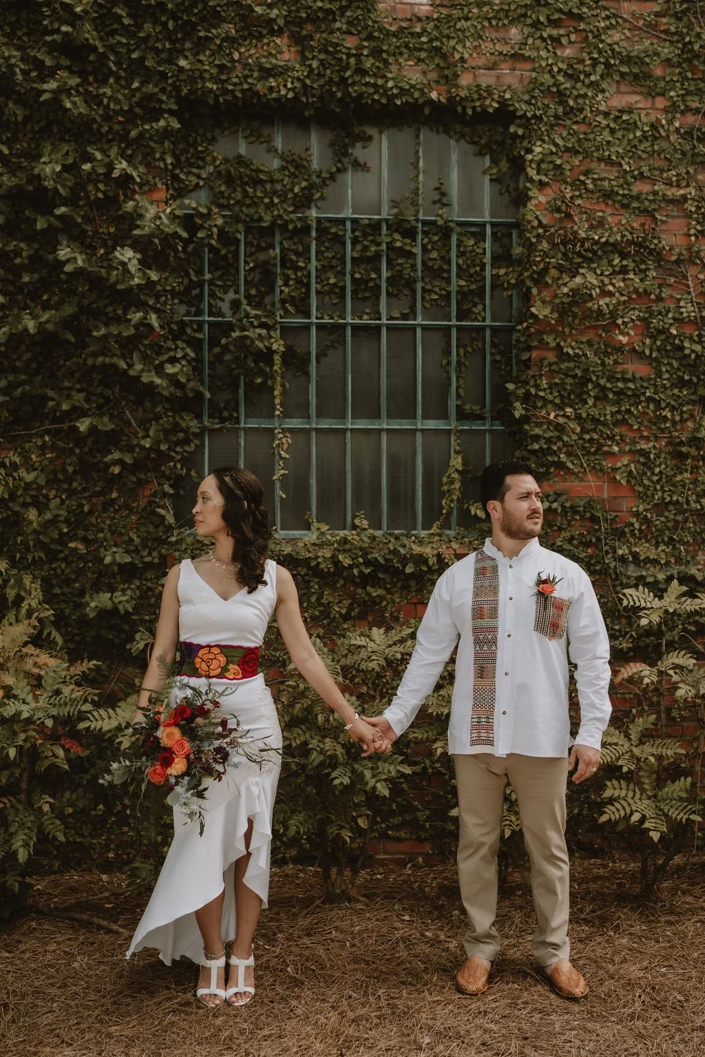 Bride and groom posing in front of the signature green ivy wall at Studio 215 in downtown Fayetteville, NC; a lush urban garden photography backdrop at our industrial warehouse venue near Fort Bragg and Raleigh.