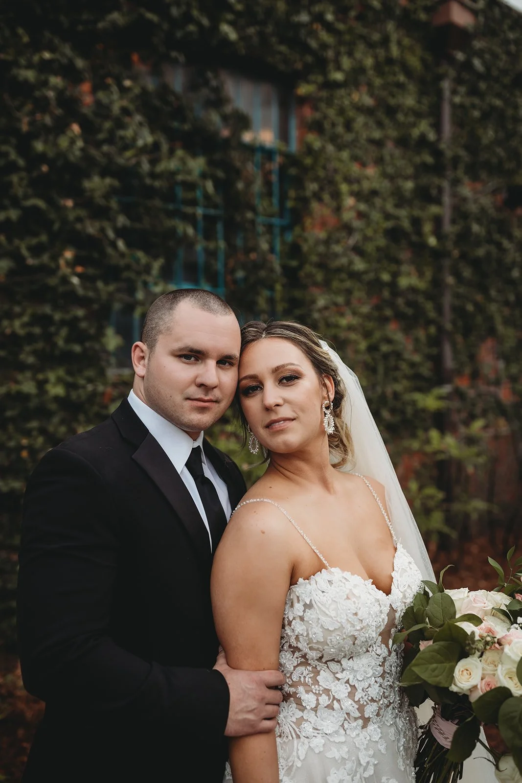 Bride and groom posing in front of the signature green ivy wall at Studio 215 in downtown Fayetteville, NC; a lush urban garden photography backdrop at our industrial warehouse venue near Fort Bragg and Raleigh.