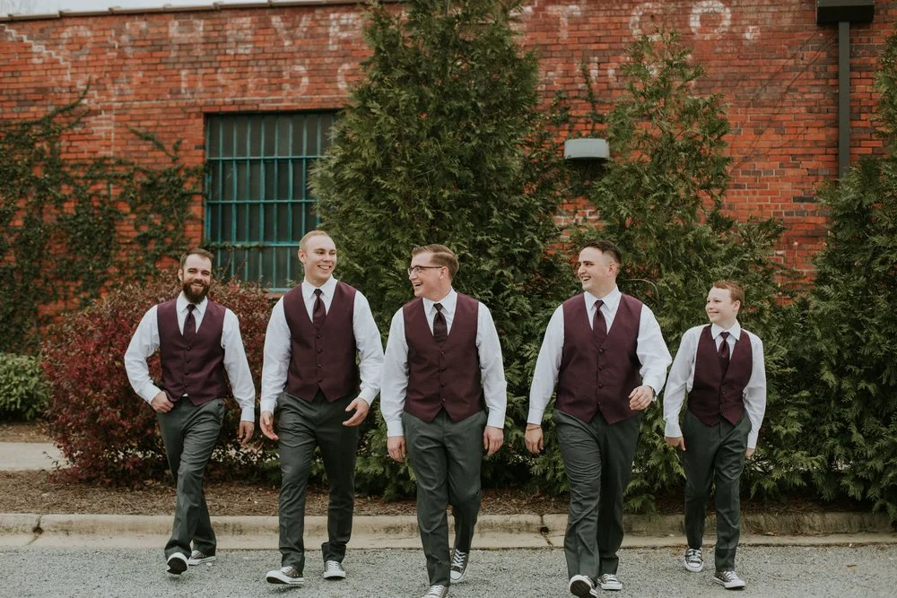 Bride and groom posing in front of the signature green ivy wall at Studio 215 in downtown Fayetteville, NC; a lush urban garden photography backdrop at our industrial warehouse venue near Fort Bragg and Raleigh.