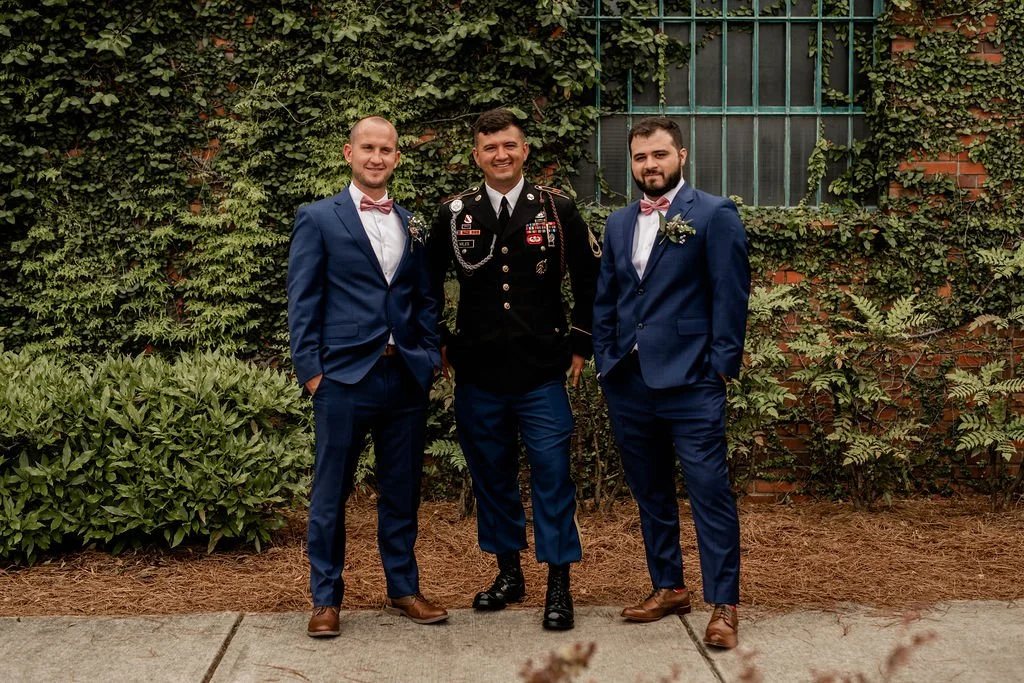 Bride and groom posing in front of the signature green ivy wall at Studio 215 in downtown Fayetteville, NC; a lush urban garden photography backdrop at our industrial warehouse venue near Fort Bragg and Raleigh.