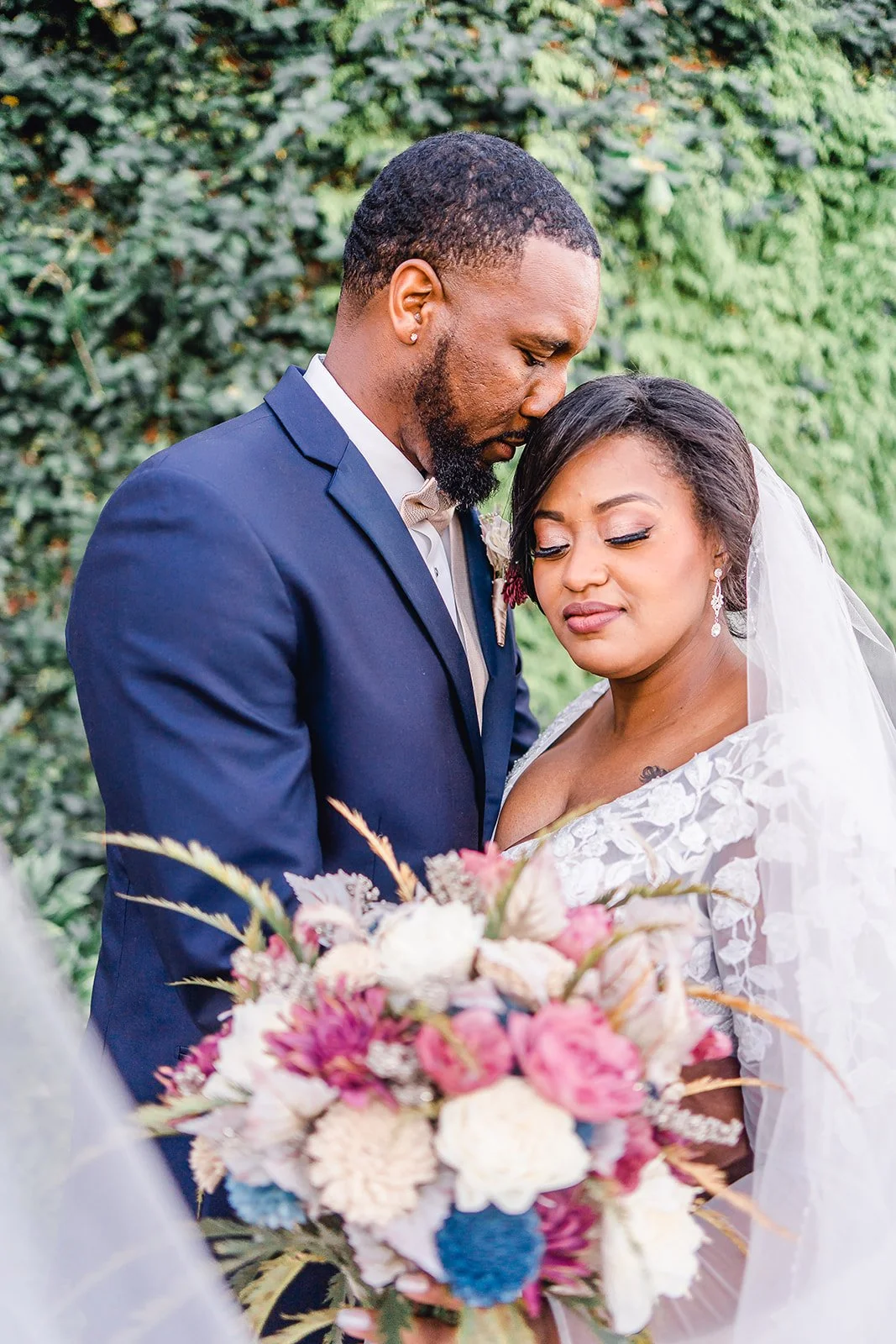 Bride and groom posing in front of the signature green ivy wall at Studio 215 in downtown Fayetteville, NC; a lush urban garden photography backdrop at our industrial warehouse venue near Fort Bragg and Raleigh.