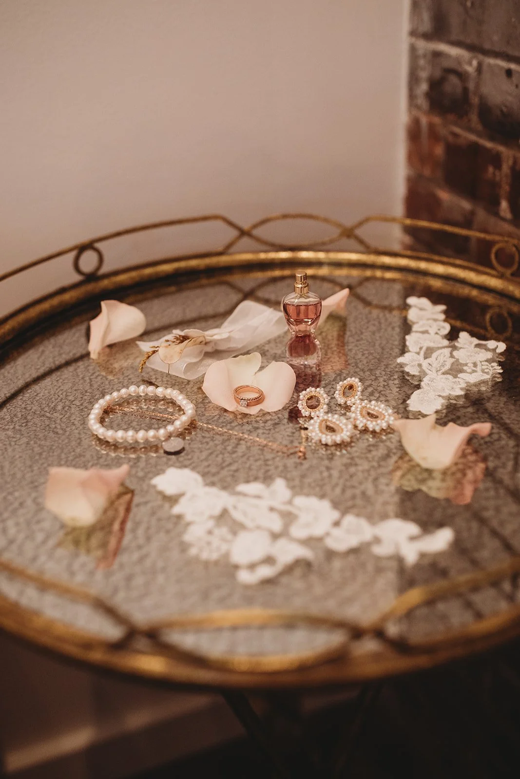 Jewelry and perfume on a decorative glass tray with scattered rose petals.
