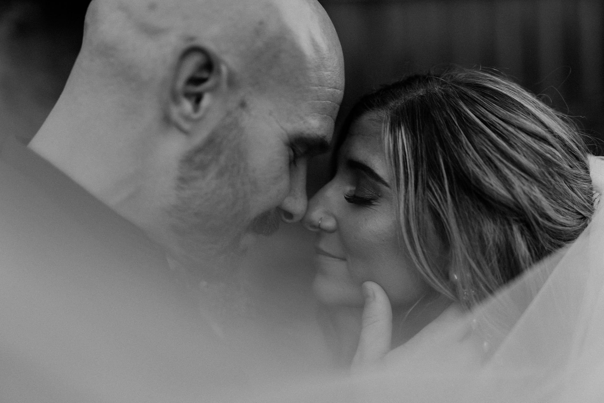 A close-up black and white photo of a man and woman touching foreheads with their eyes closed, sharing an intimate moment.