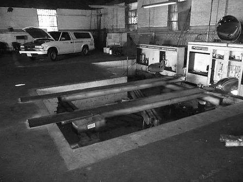 Underground parking lot with wooden planks covering an opened maintenance access hatch and parked vehicles in the background