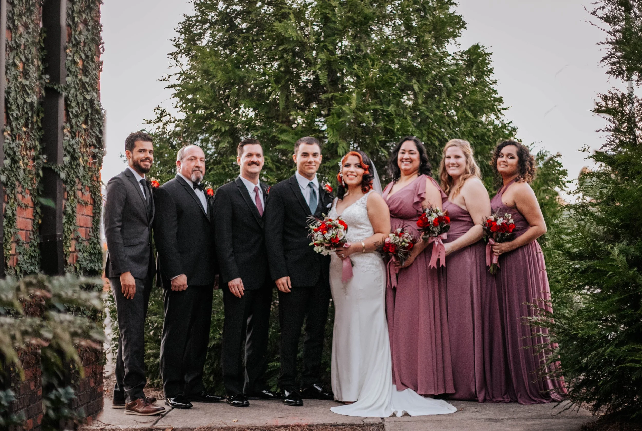Bride and groom posing in front of the signature green ivy wall at Studio 215 in downtown Fayetteville, NC; a lush urban garden photography backdrop at our industrial warehouse venue near Fort Bragg and Raleigh.