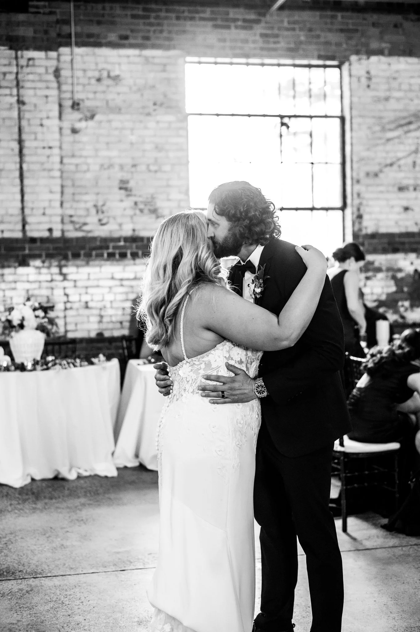 A bride and groom sharing a kiss on their wedding dance floor in a rustic indoor setting.