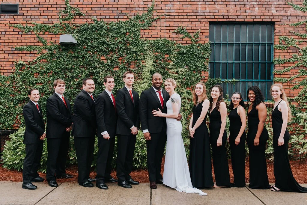 Bride and groom posing in front of the signature green ivy wall at Studio 215 in downtown Fayetteville, NC; a lush urban garden photography backdrop at our industrial warehouse venue near Fort Bragg and Raleigh.