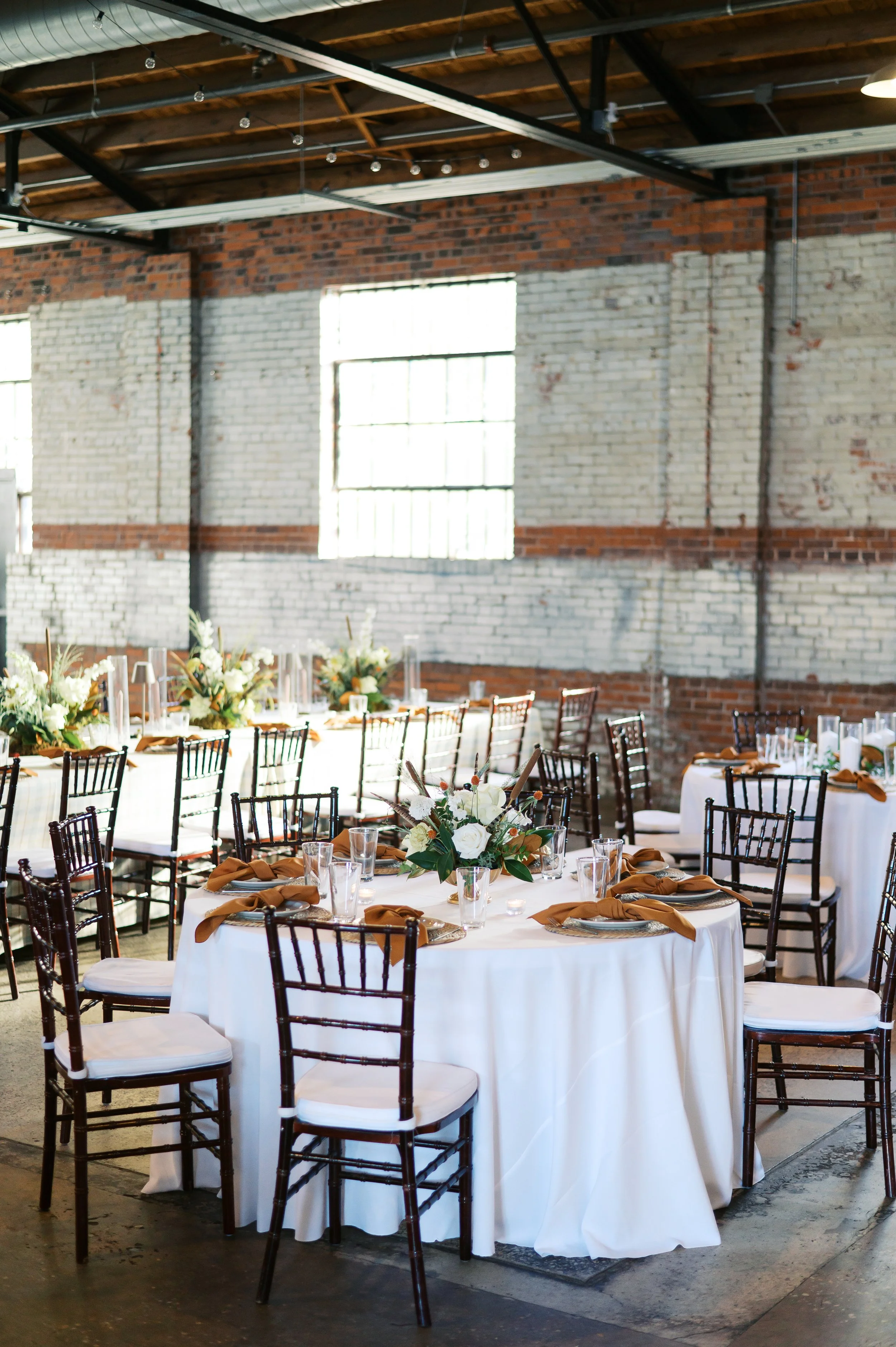 A large industrial wedding ceremony space at Studio 215 in Fayetteville, NC, featuring original 1937 exposed brick walls, vaulted wood ceilings, and steel cross-bow beams.
