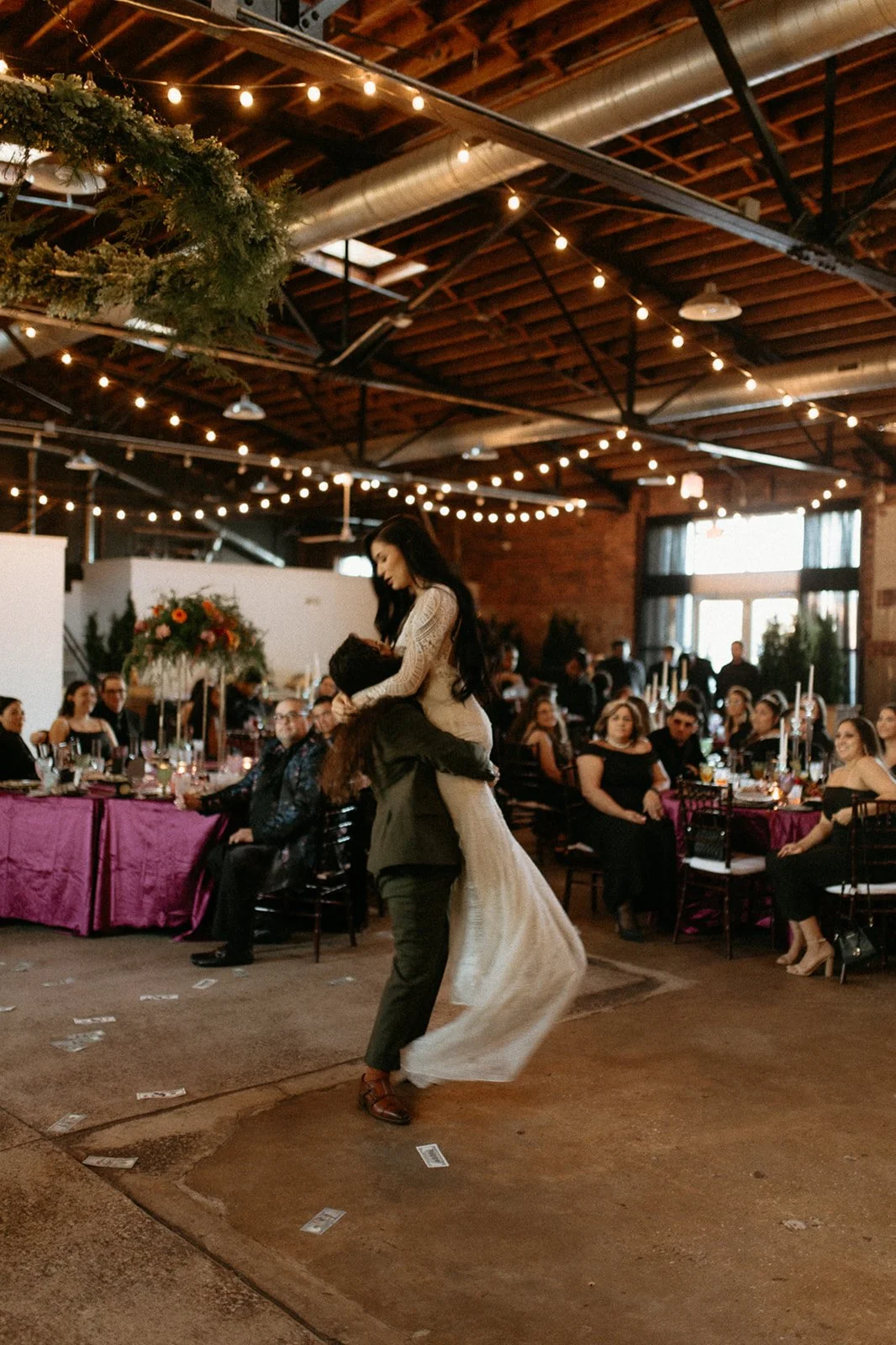 Couple dancing at a wedding reception inside a decorated venue with string lights, tables with pink tablecloths, and guests watching. at Studio 215 a modern warehouse venue in Fayetteville, NC