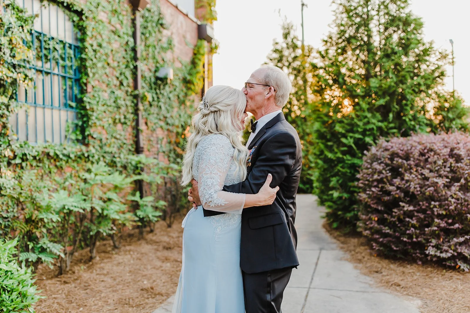 Bride and groom posing in front of the signature green ivy wall at Studio 215 in downtown Fayetteville, NC; a lush urban garden photography backdrop at our industrial warehouse venue near Fort Bragg and Raleigh.