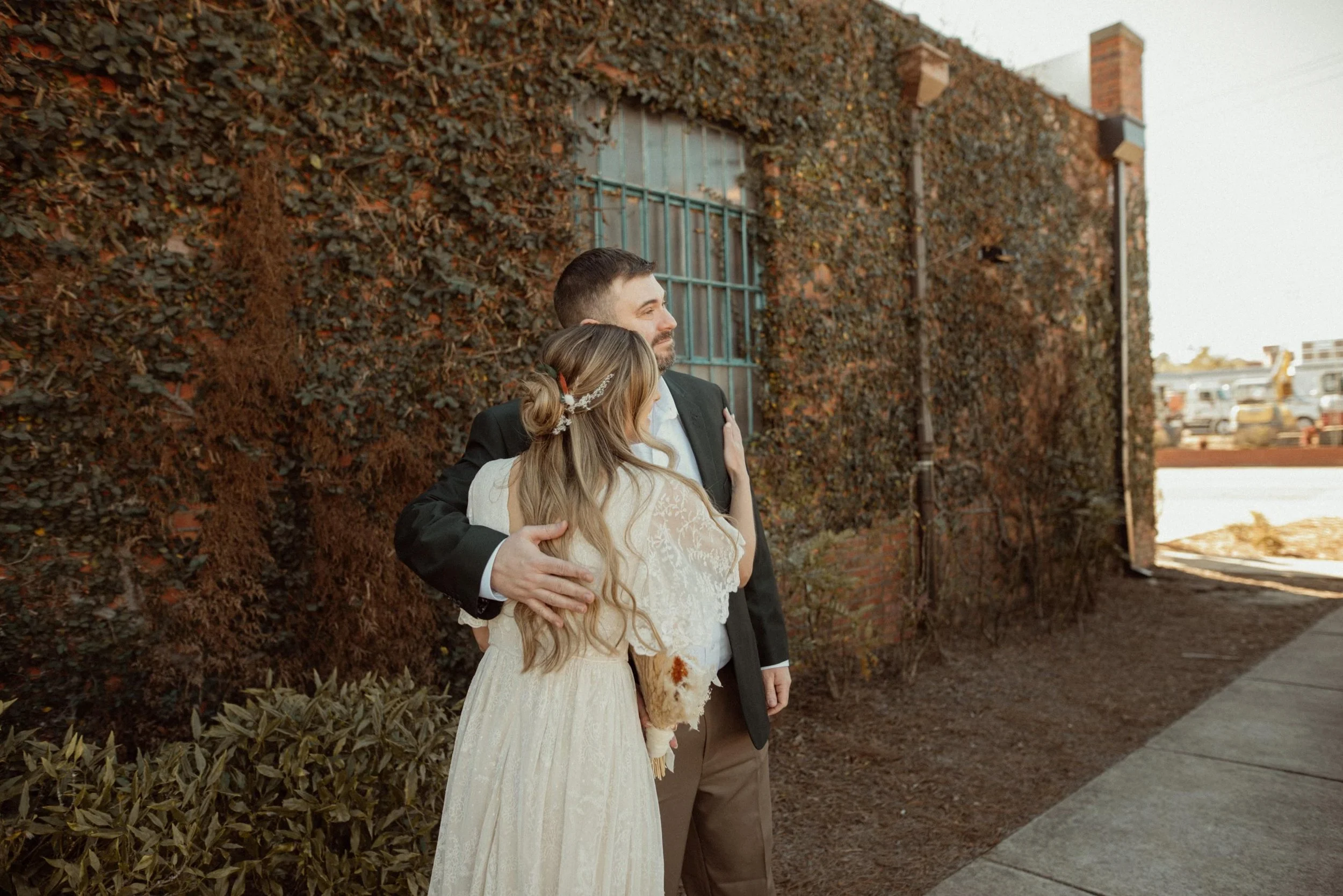 Bride and groom posing in front of the signature green ivy wall at Studio 215 in downtown Fayetteville, NC; a lush urban garden photography backdrop at our industrial warehouse venue near Fort Bragg and Raleigh.