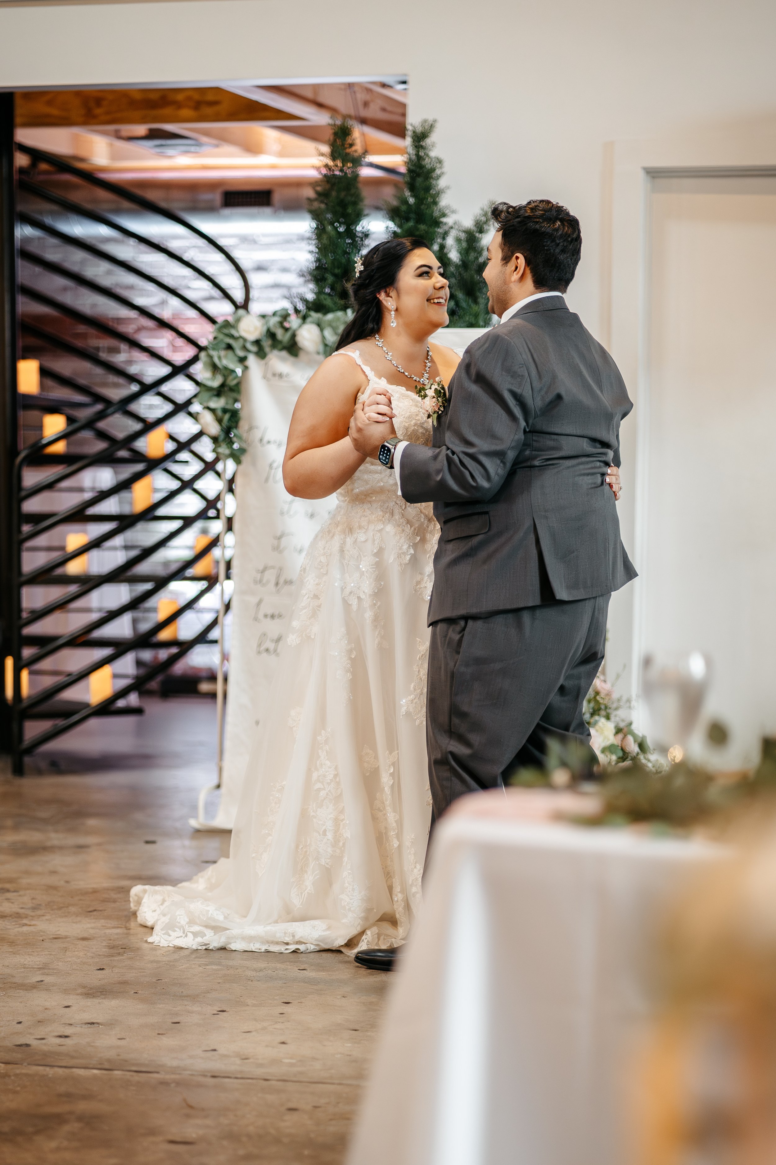 A bride and groom share their first dance at a wedding reception, smiling and holding each other.