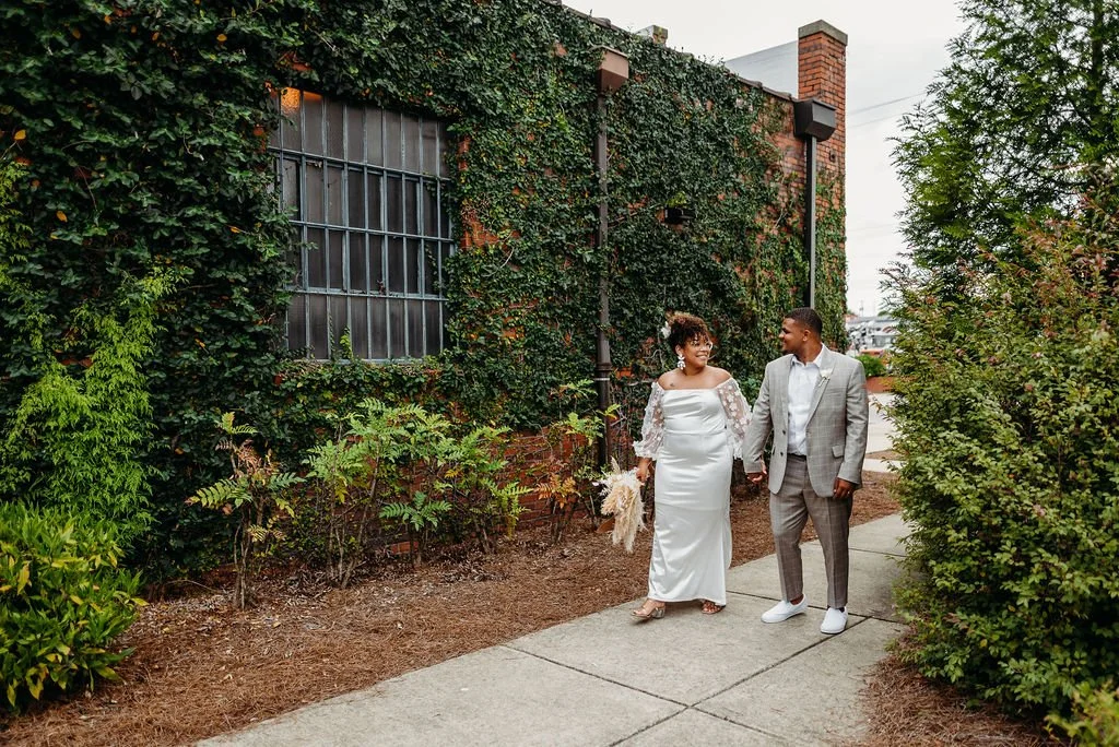 Bride and groom posing in front of the signature green ivy wall at Studio 215 in downtown Fayetteville, NC; a lush urban garden photography backdrop at our industrial warehouse venue near Fort Bragg and Raleigh.
