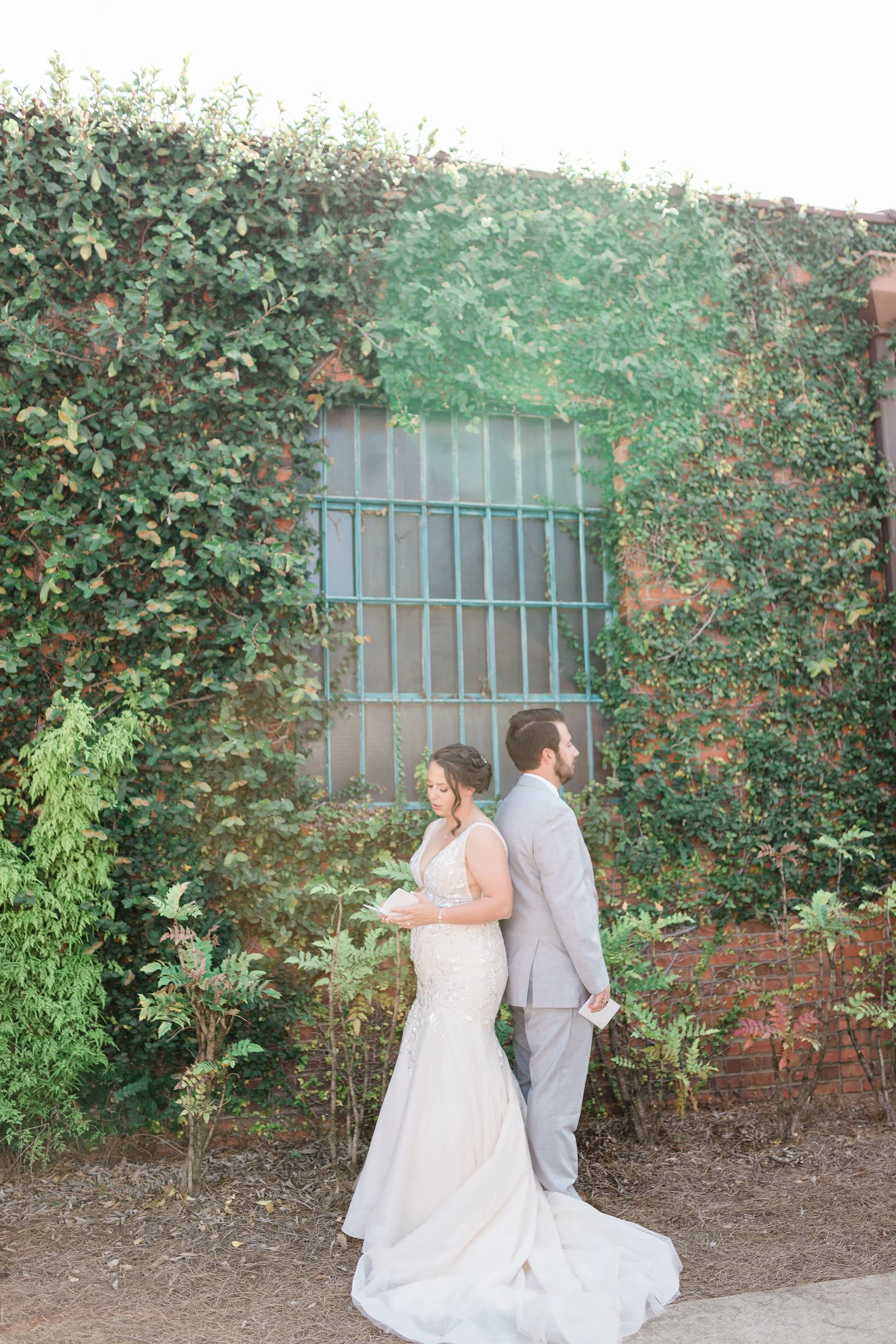 Bride and groom posing in front of the signature green ivy wall at Studio 215 in downtown Fayetteville, NC; a lush urban garden photography backdrop at our industrial warehouse venue near Fort Bragg and Raleigh.
