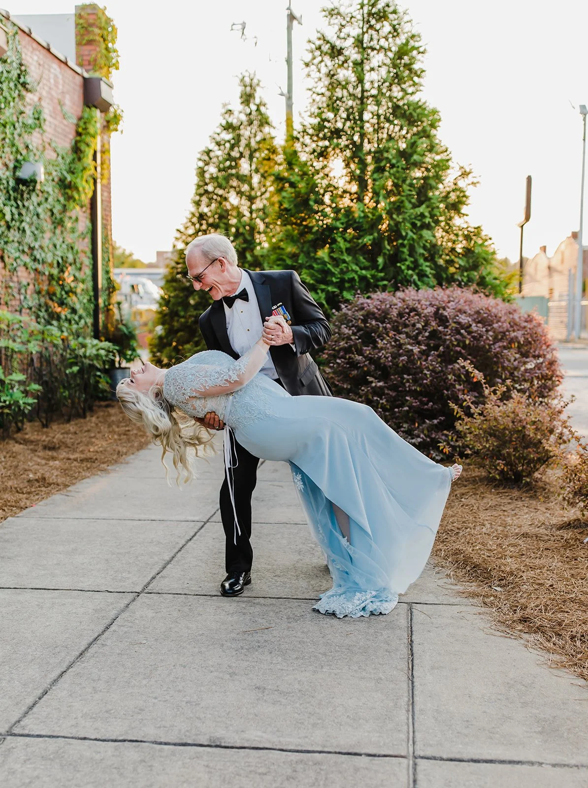 Bride and groom posing in front of the signature green ivy wall at Studio 215 in downtown Fayetteville, NC; a lush urban garden photography backdrop at our industrial warehouse venue near Fort Bragg and Raleigh.