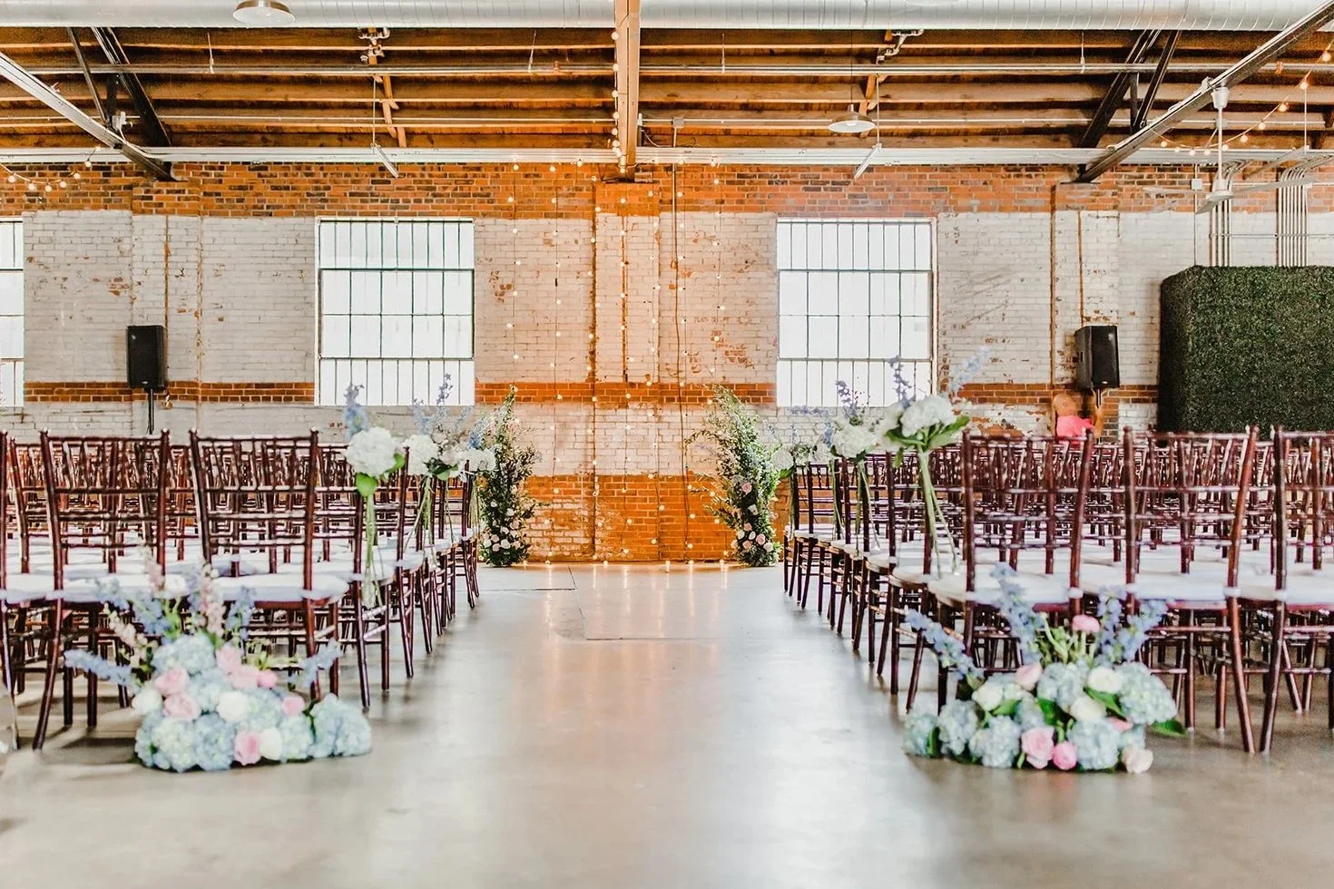 A large industrial wedding ceremony space at Studio 215 in Fayetteville, NC, featuring original 1937 exposed brick walls, vaulted wood ceilings, and steel cross-bow beams.