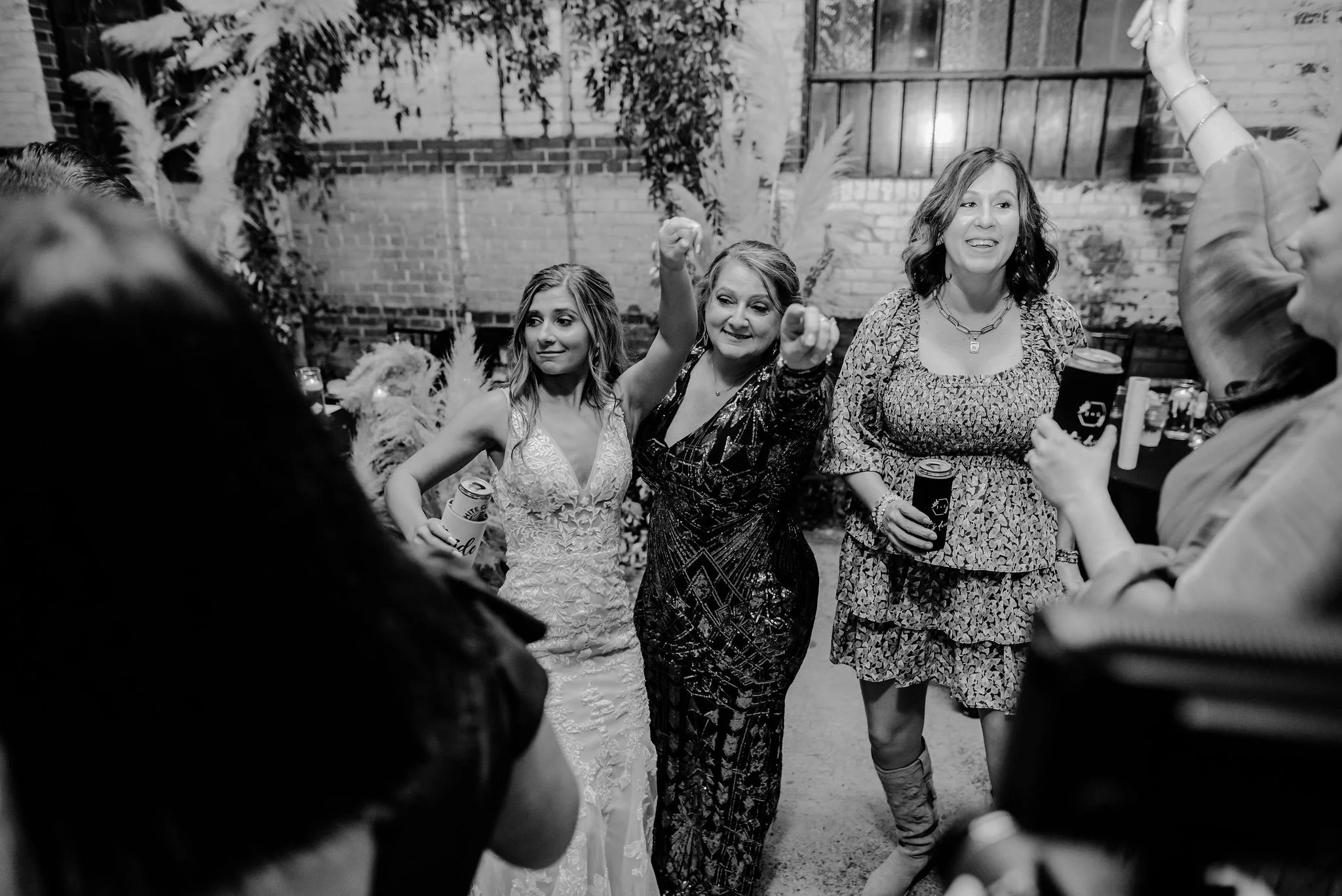 People dancing and celebrating outdoors at a social gathering or party, with a brick wall and plants in the background.