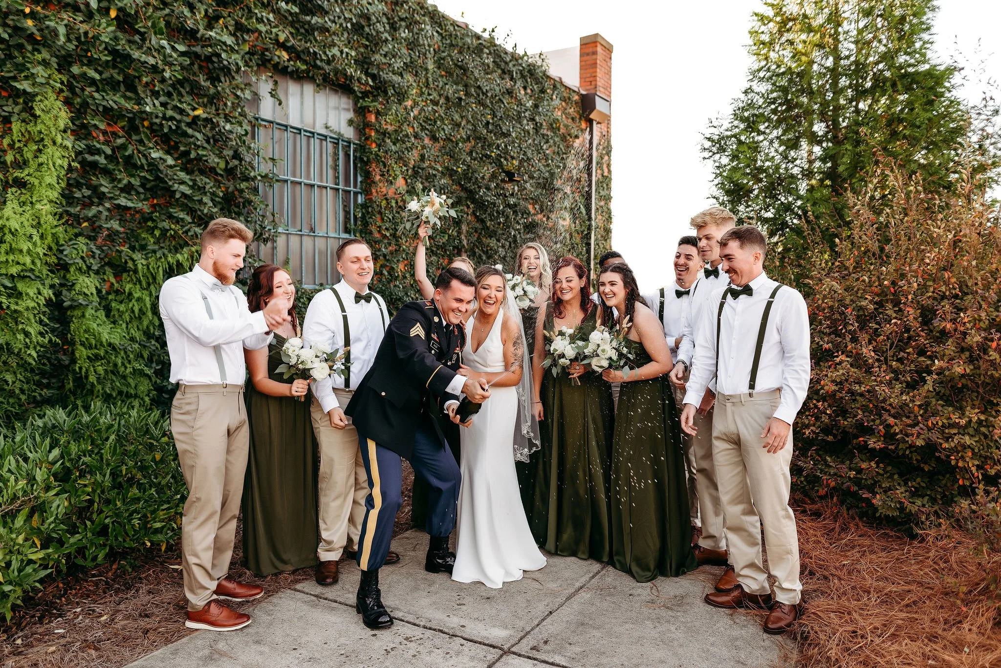 Bride and groom posing in front of the signature green ivy wall at Studio 215 in downtown Fayetteville, NC; a lush urban garden photography backdrop at our industrial warehouse venue near Fort Bragg and Raleigh.