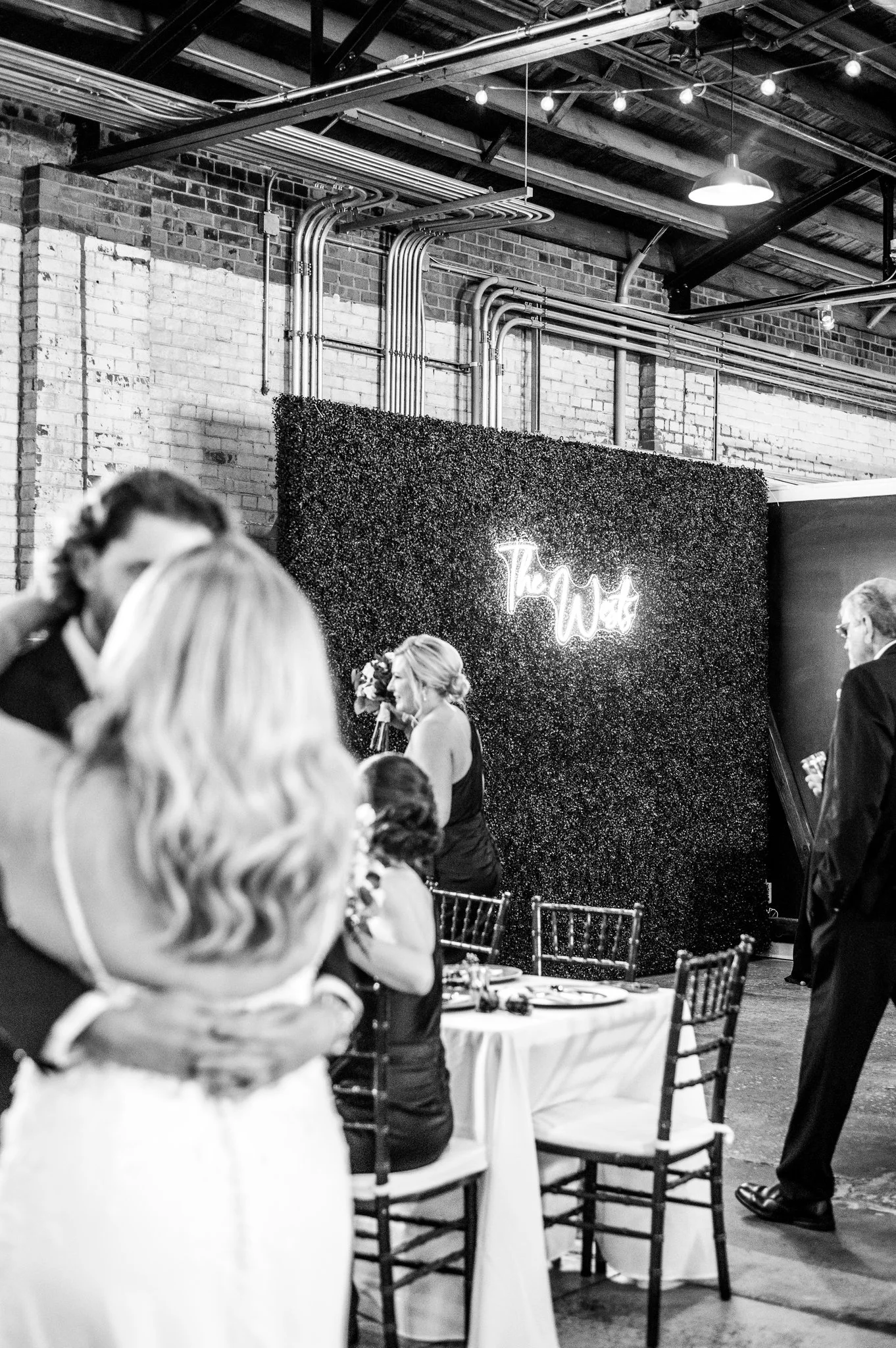 People at a reception with a decorated wall and neon sign saying "The Wild."