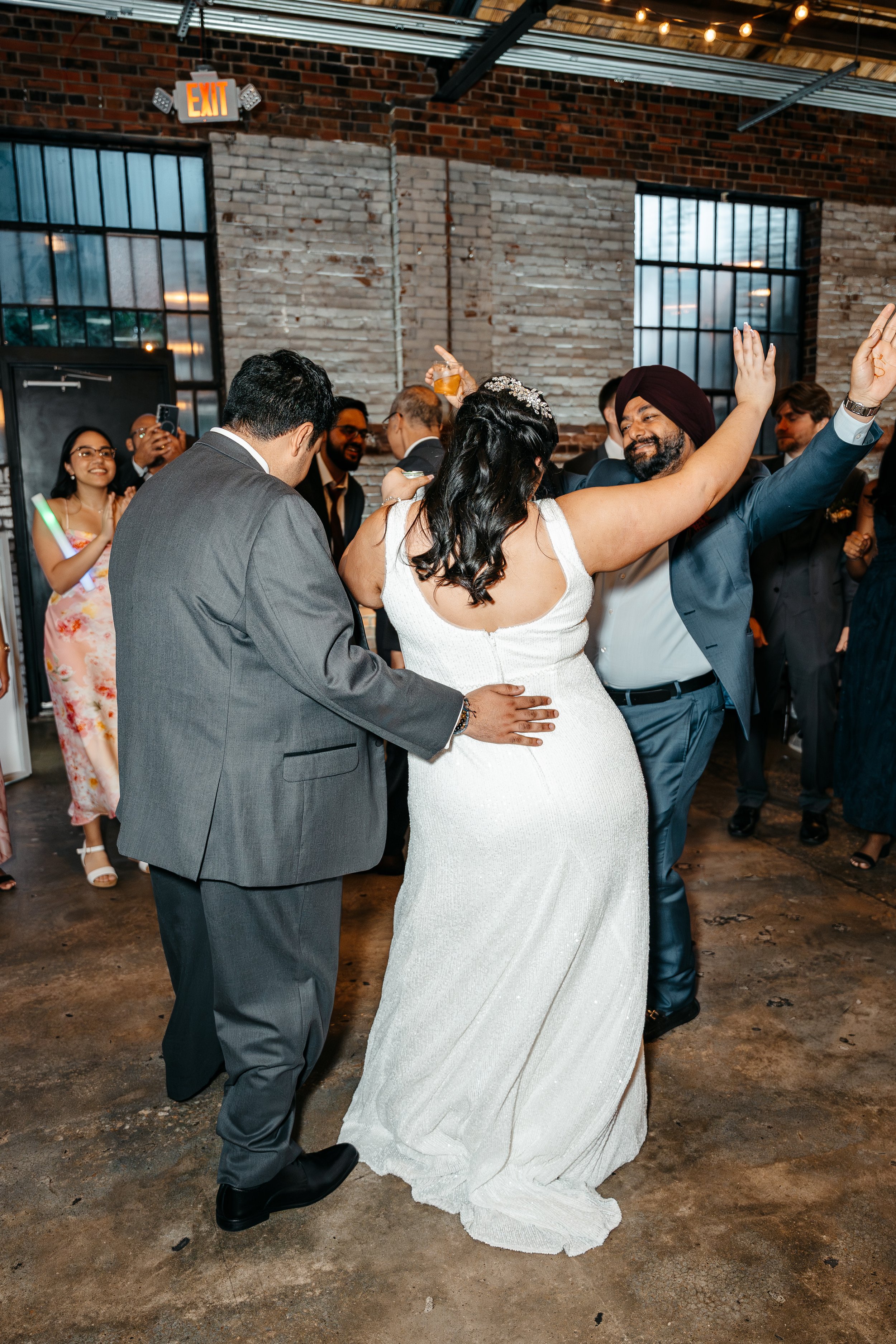 Modern warehouse wedding venue Studio 215 in Fayetteville NC. With exposed brick, dancing guests, a bride and groom dancing, happy.