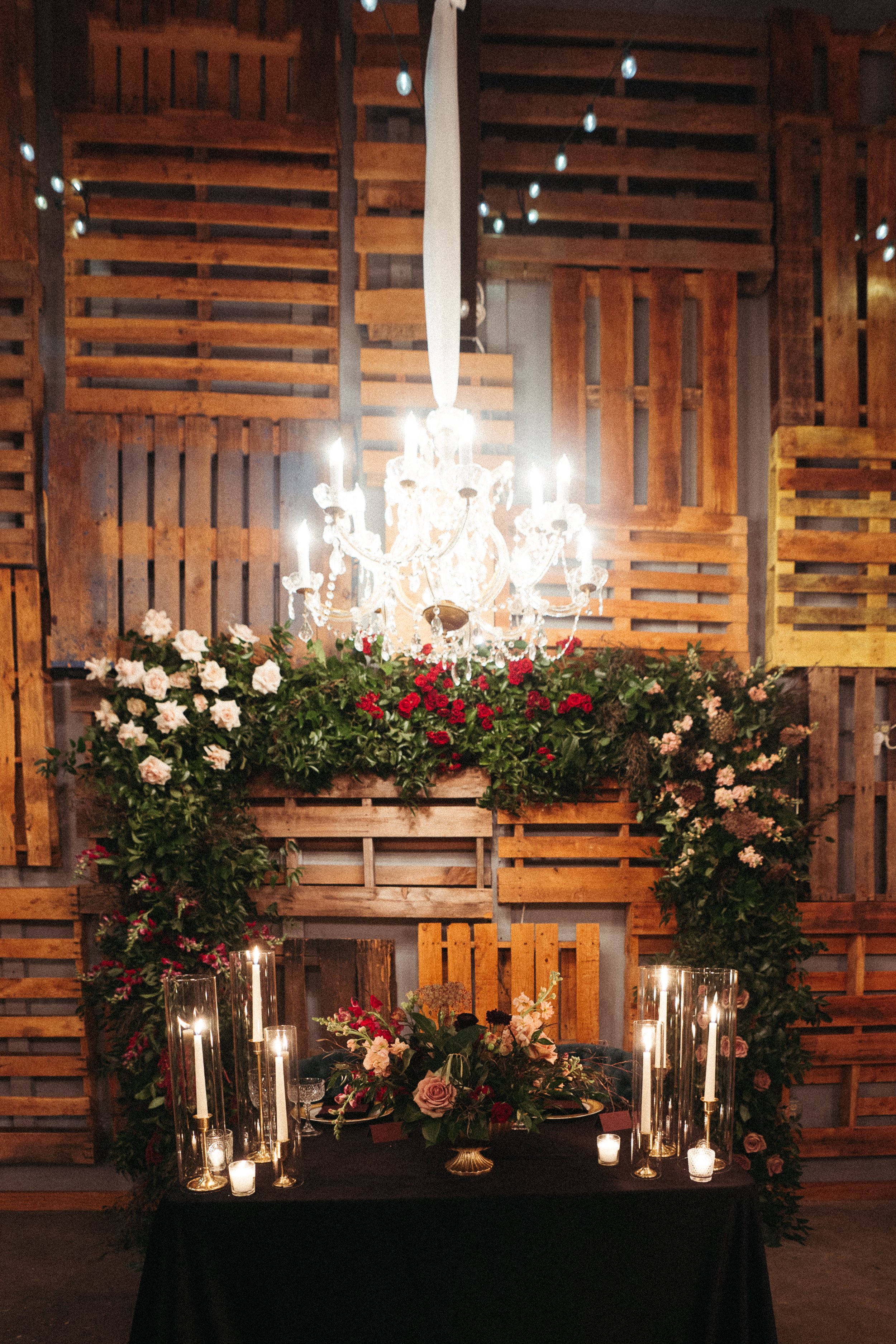 Elegant indoor event space with a chandelier chandelier, floral arrangements, candles, and wooden decor background.
