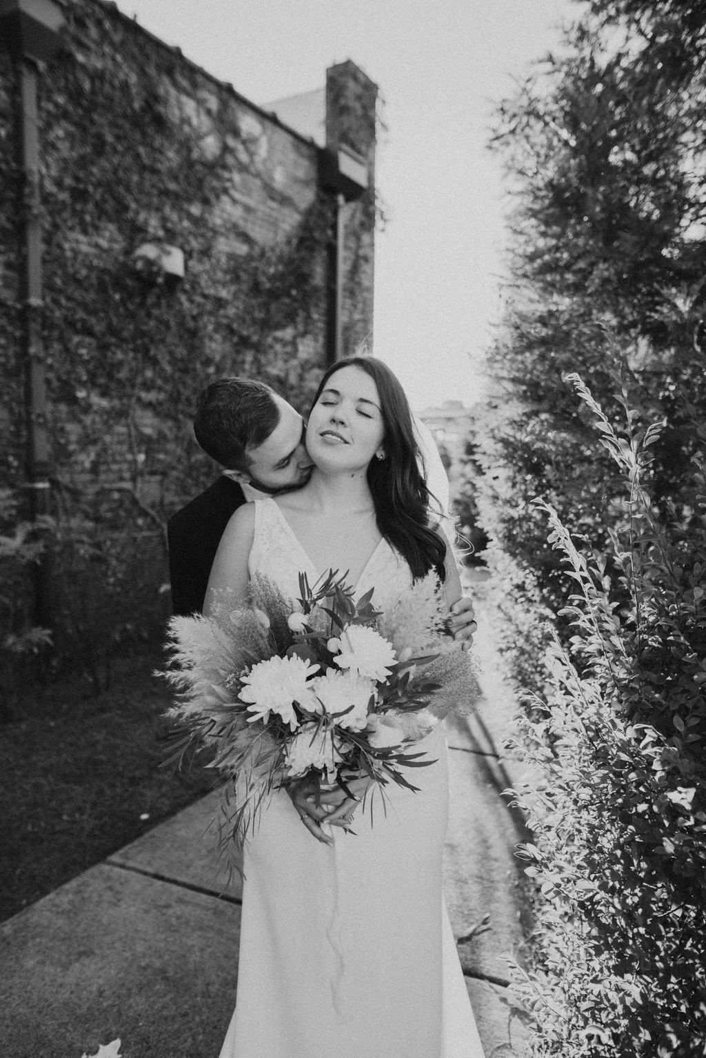 Bride and groom posing in front of the signature green ivy wall at Studio 215 in downtown Fayetteville, NC; a lush urban garden photography backdrop at our industrial warehouse venue near Fort Bragg and Raleigh.