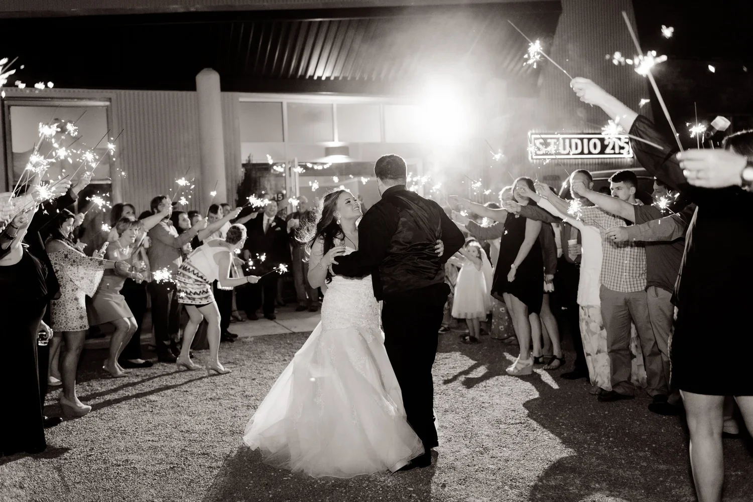 A bride and groom dancing together at their wedding reception, surrounded by guests holding sparklers in a nighttime outdoor setting.