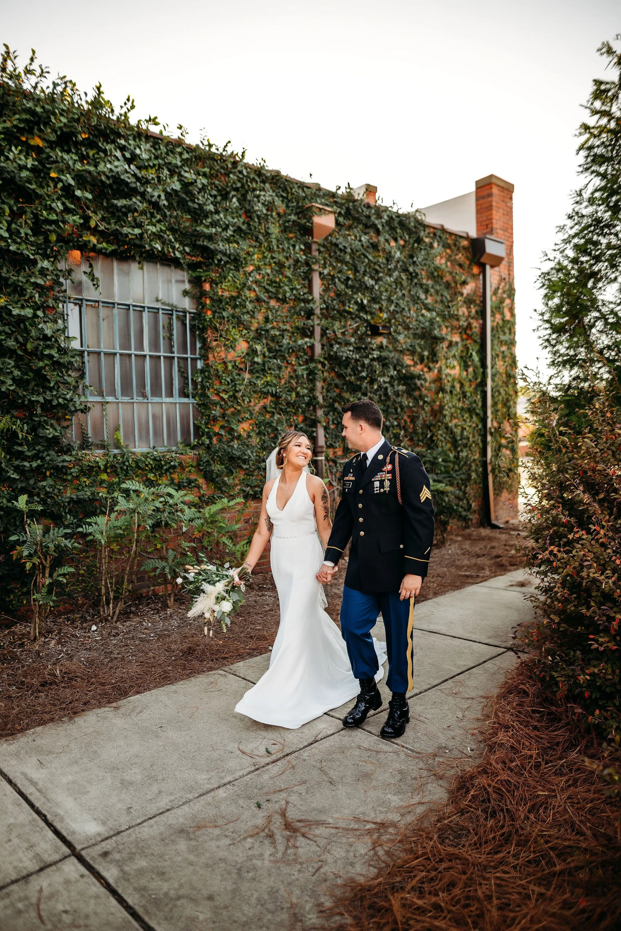 Bride and groom posing in front of the signature green ivy wall at Studio 215 in downtown Fayetteville, NC; a lush urban garden photography backdrop at our industrial warehouse venue near Fort Bragg and Raleigh.