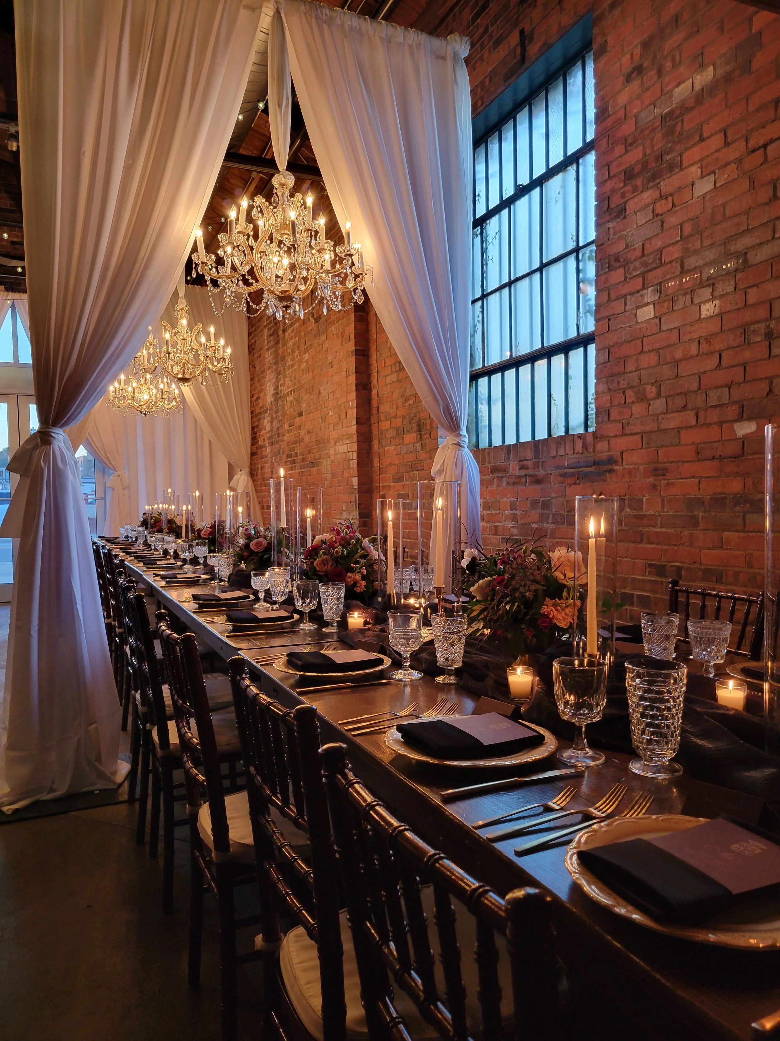 industrial chic event space at Studio 215 in Fayetteville, NC, featuring exposed brick walls, hanging  drapery and rented chandeliers and floral with candlescenterpieces for a baby shower or bridal shower