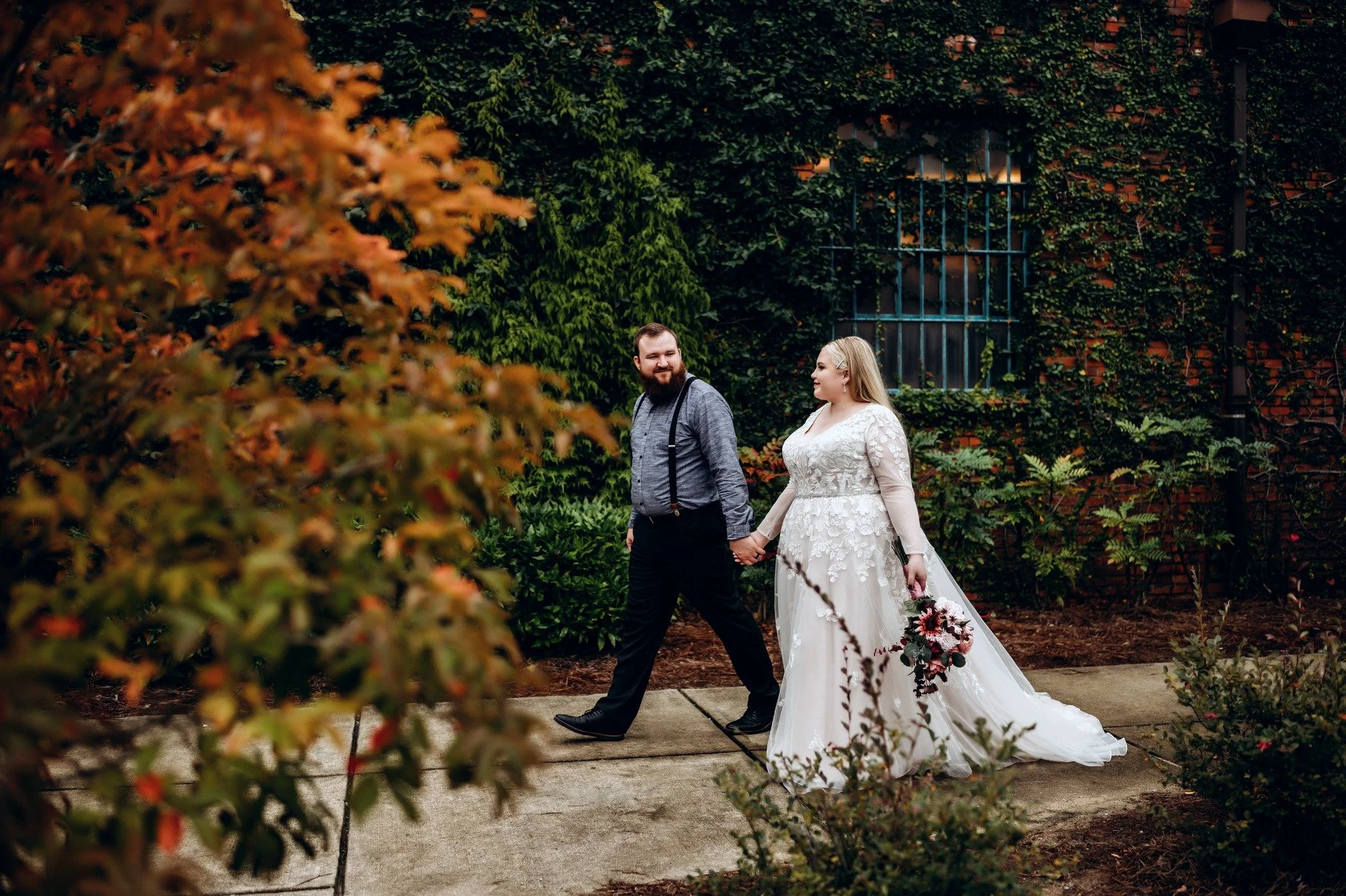 Bride and groom posing in front of the signature green ivy wall at Studio 215 in downtown Fayetteville, NC; a lush urban garden photography backdrop at our industrial warehouse venue near Fort Bragg and Raleigh.