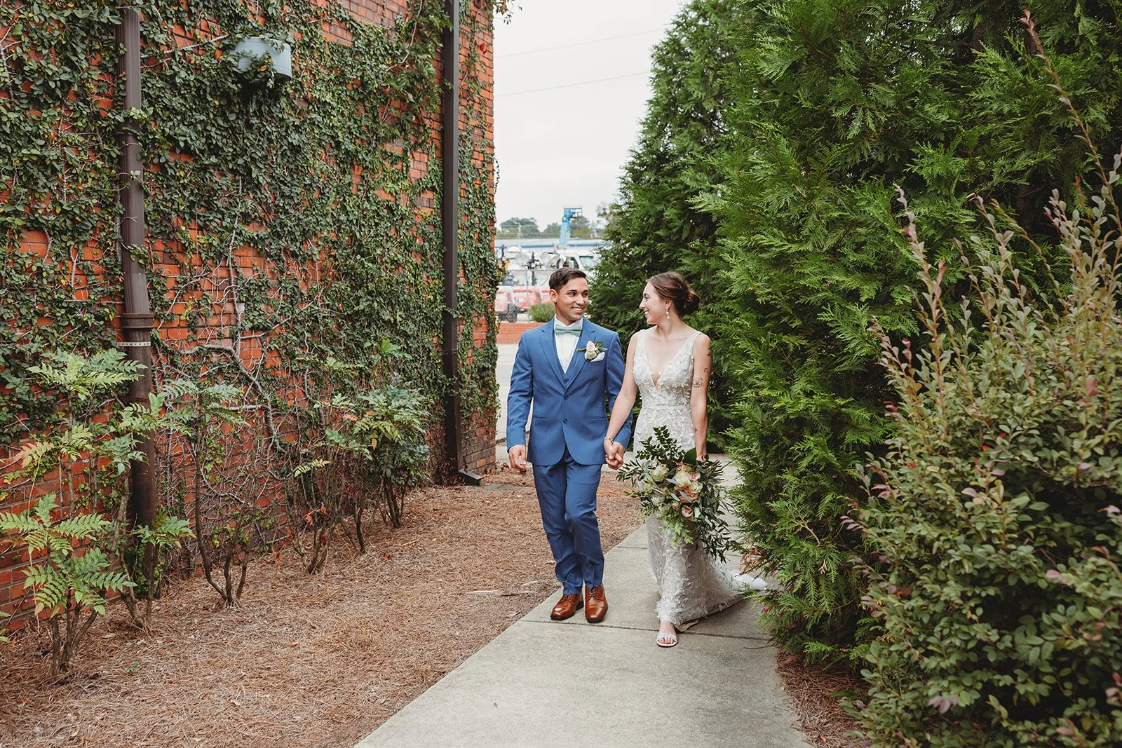 Bride and groom posing in front of the signature green ivy wall at Studio 215 in downtown Fayetteville, NC; a lush urban garden photography backdrop at our industrial warehouse venue near Fort Bragg and Raleigh.
