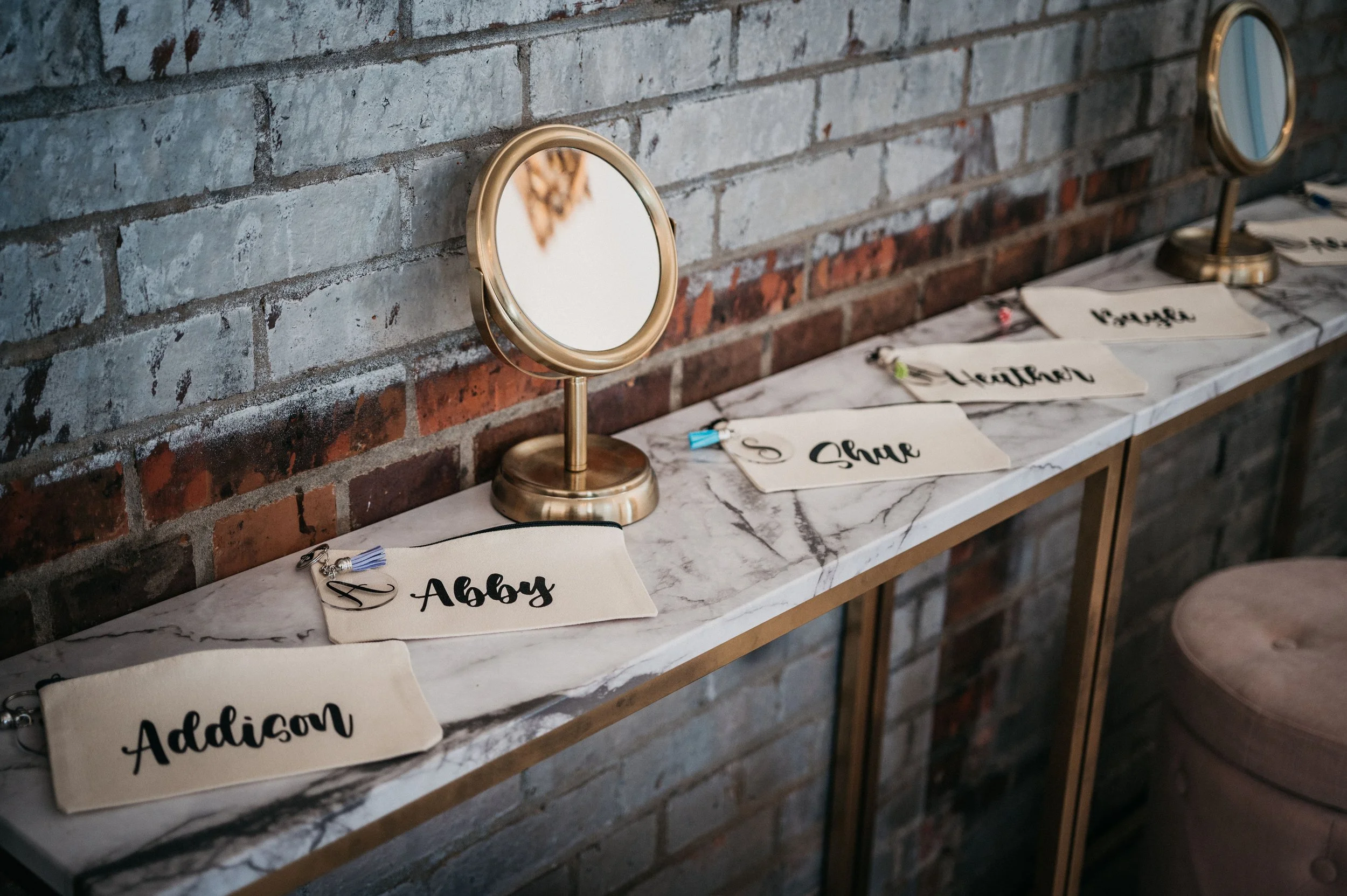 Name tags for guests, including Addison, Abby, and others, are arranged on a marble-topped table against an exposed brick wall. Small mirrors are placed behind the tags.