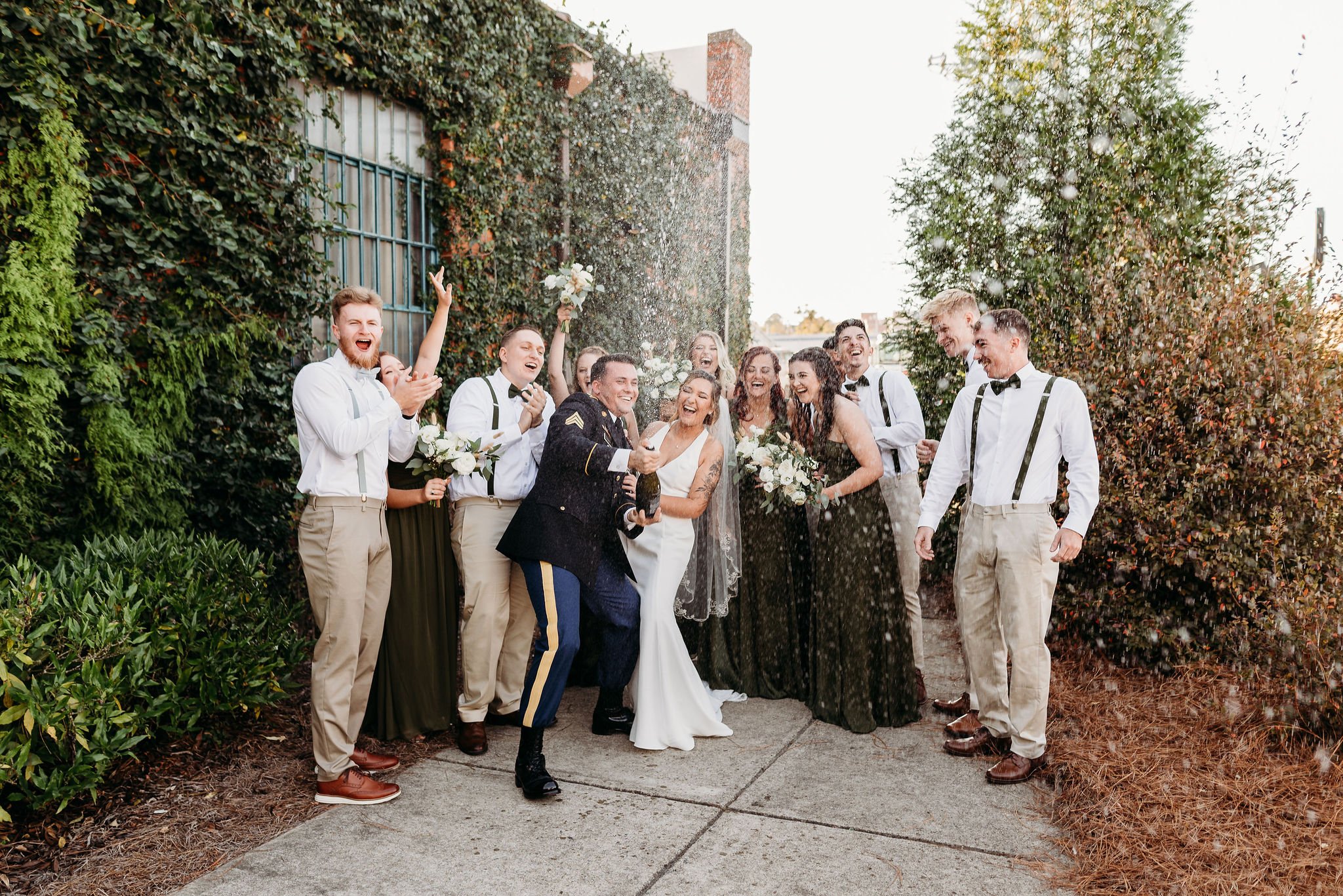 Group of people celebrating and throwing confetti outdoors, with a bride and groom in the center, everyone dressed in formal attire. at Studio 215 a modern warehouse wedding venue in Fayetteville, NC