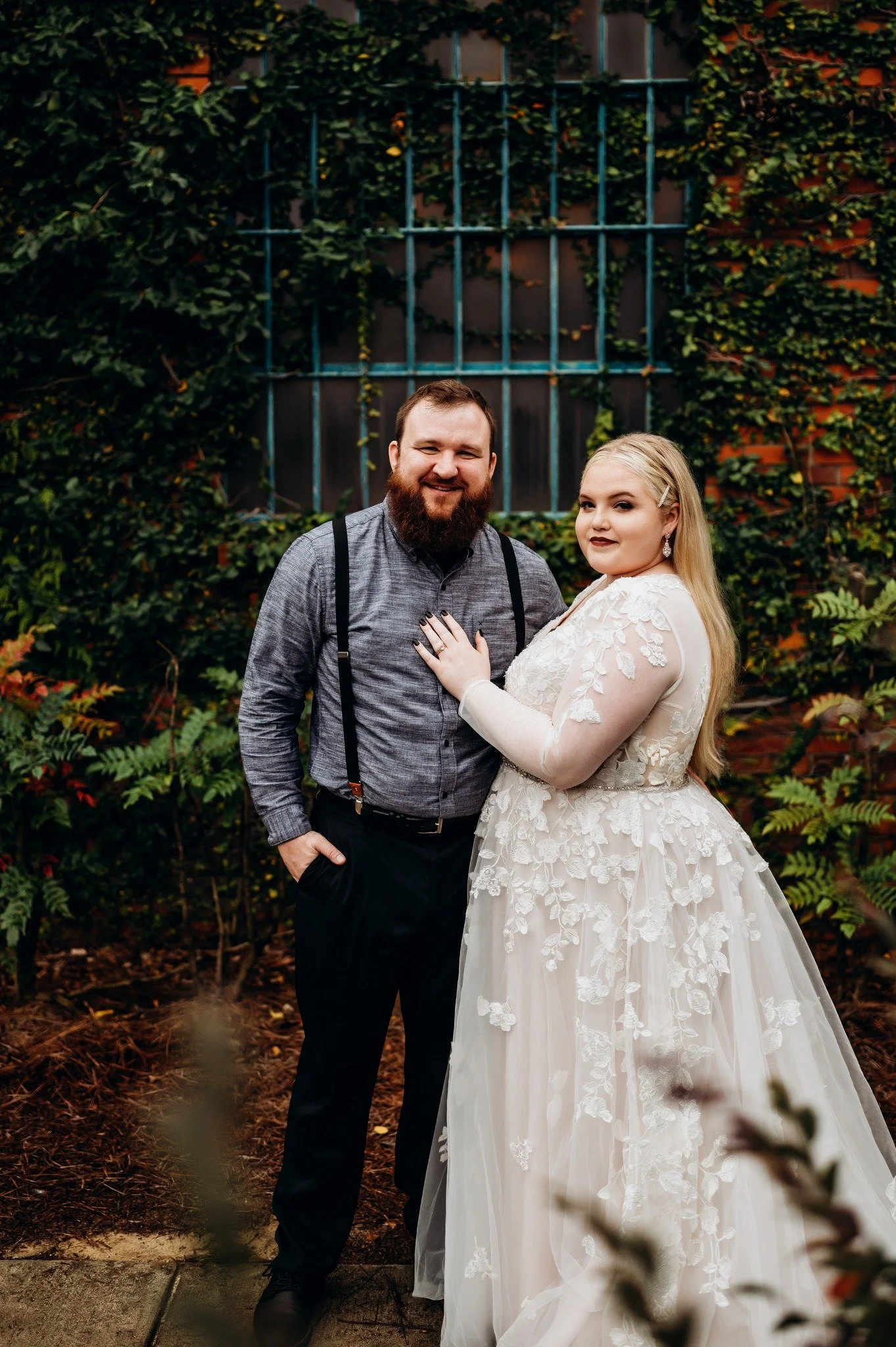 Bride and groom posing in front of the signature green ivy wall at Studio 215 in downtown Fayetteville, NC; a lush urban garden photography backdrop at our industrial warehouse venue near Fort Bragg and Raleigh.
