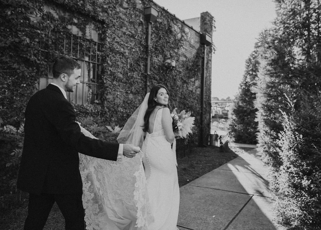 Bride and groom posing in front of the signature green ivy wall at Studio 215 in downtown Fayetteville, NC; a lush urban garden photography backdrop at our industrial warehouse venue near Fort Bragg and Raleigh.