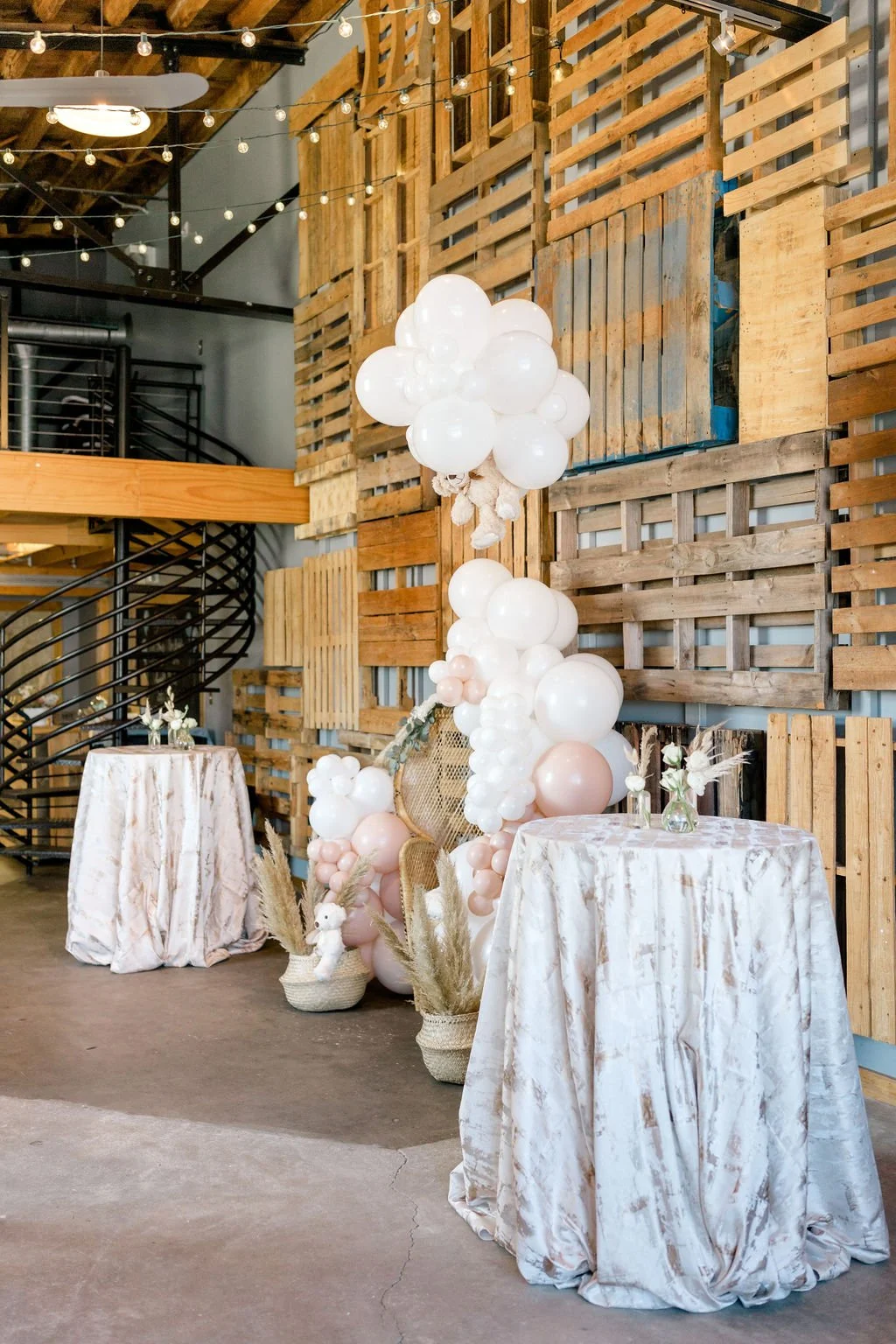 Rustic baby shower at Fayetteville NC boutique venue at Studio 215. Image features a 25 ft tall wood focal backdrop wall,  a whicker thrown chair, blush and white balloons, and small floral centerpieces